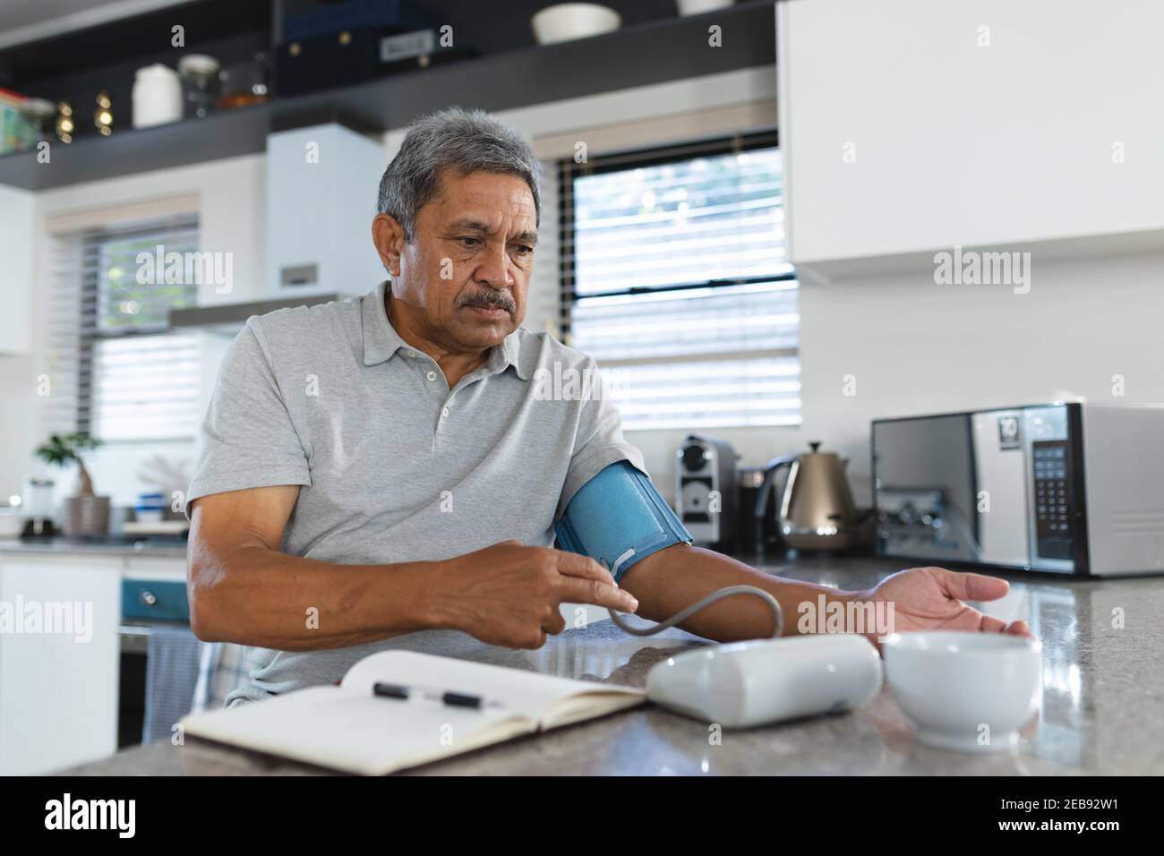 Uomo di razza misto senior a casa prendendo la sua pressione sanguigna in cucina Foto Stock