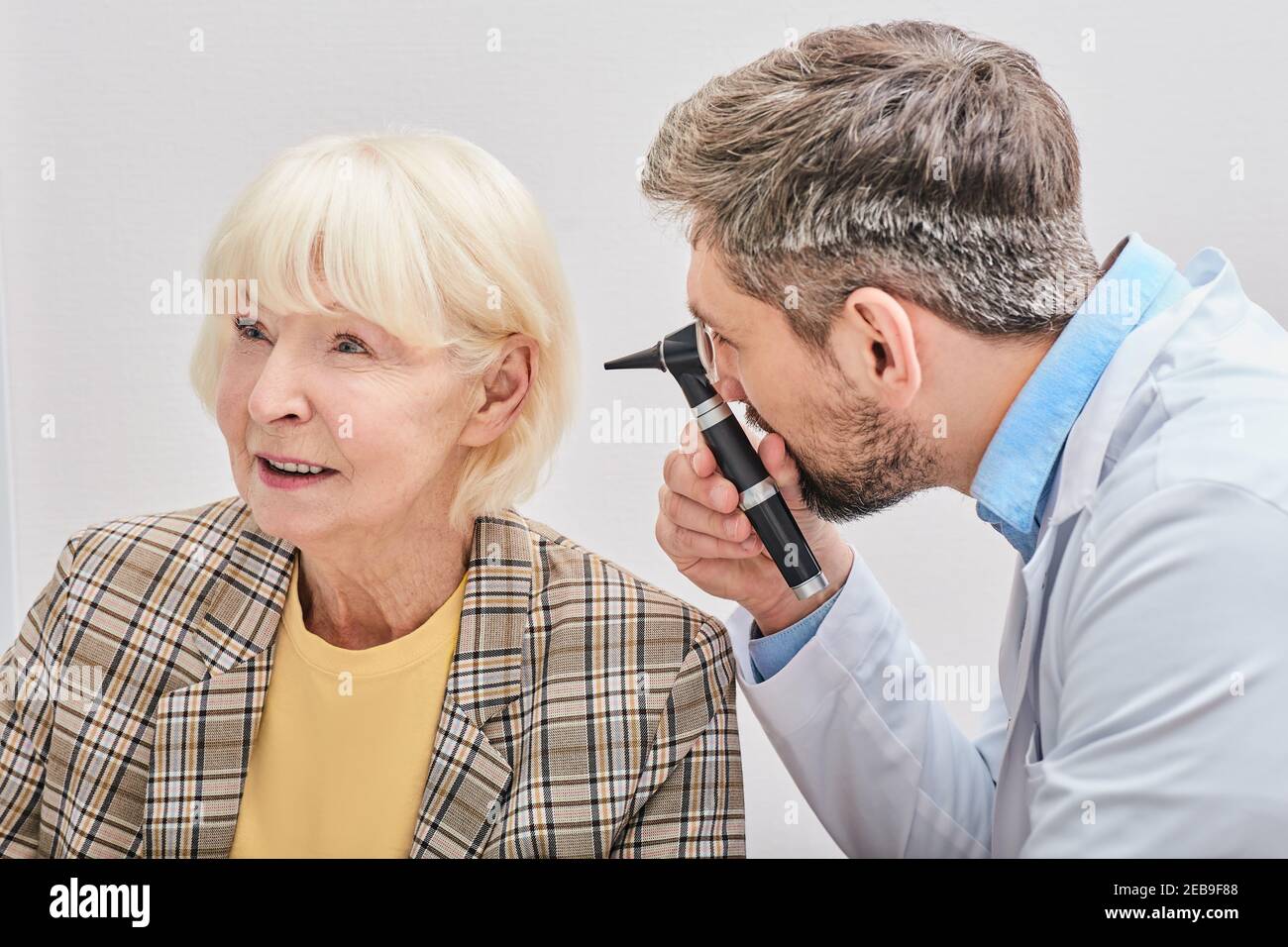 ENT medico che controlla l'orecchio femminile anziano usando un otoscopio. Esame uditivo per donna anziana. Otite media, infiammazione dell'orecchio Foto Stock
