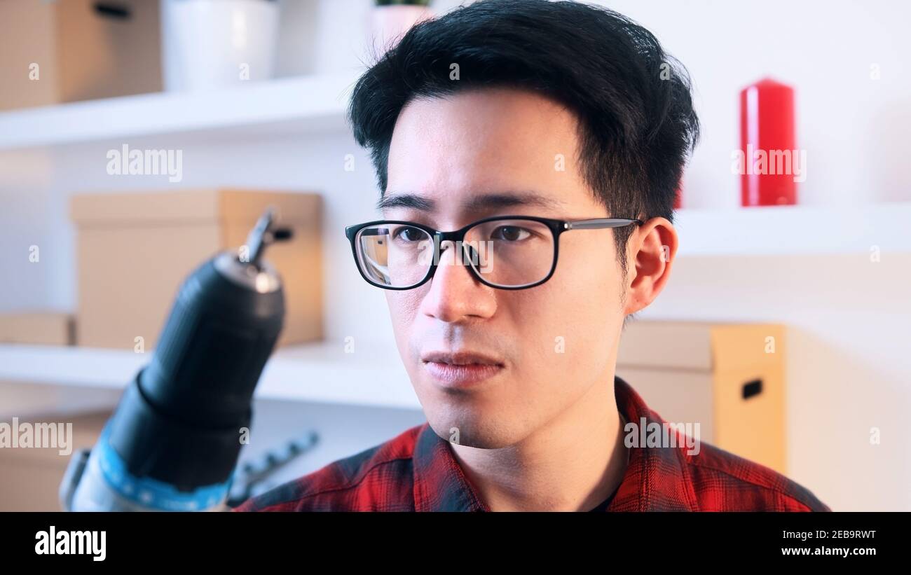 Confuso l'uomo asiatico con gli occhiali che tengono il trapano. Foto di alta qualità Foto Stock