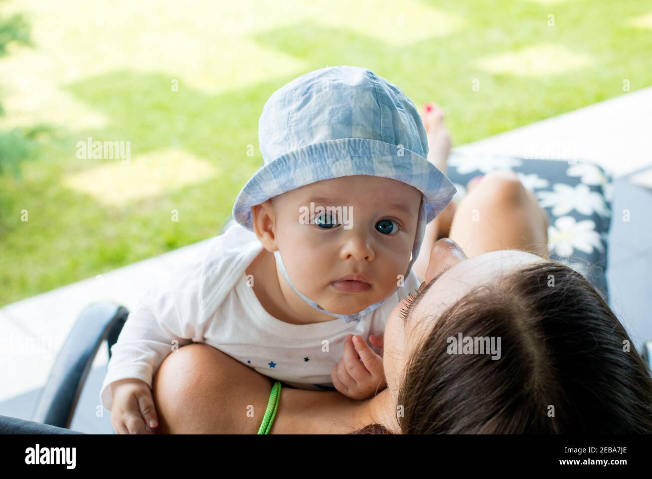 Bambino che riposa sopra la spalla della madre e guarda fuori con occhi blu focalizzati espressione curiosa Foto Stock