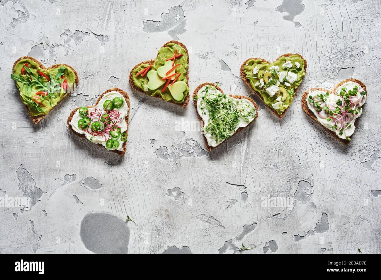 Selezione gourmet di cicchetti a forma di cuore, tartine o tapas su pane di segale con pera di avocado fresca, erbe verdi fresche e peperoncino in un bordo superiore Foto Stock