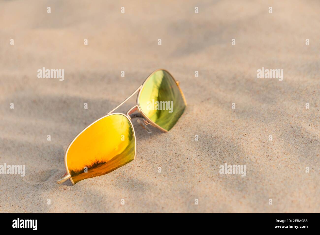 Occhiali da sole sulla spiaggia che riflettono le dune di sabbia. Occhiali da sole a specchio sulla spiaggia di sabbia nel giorno d'estate. Occhiali da sole sulla sabbia come concetto di vacanza estiva. Foto Stock