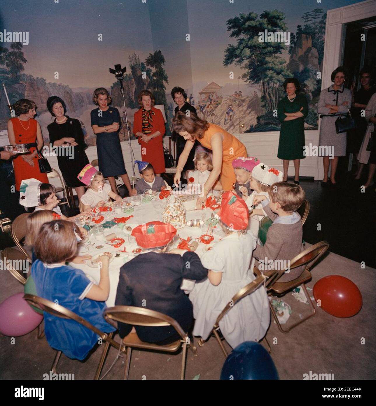 Festa di compleanno per Caroline Kennedy e John F. Kennedy, Jr. La First Lady Jacqueline Kennedy colloca la torta di Caroline Kennedyu0027s sul tavolo durante una festa di compleanno congiunta per Caroline e John F. Kennedy, Jr. Avery Hatcher, figlio del Segretario della Stampa associato, Andrew T. Hatcher, siede a sinistra di Caroline; Maria Shriver (con retro alla telecamera) siede a sinistra in primo piano; Janet Auchincloss (secondo da sinistra) si trova dietro. Presidentu2019s Dining Room (Residence), Casa Bianca, Washington, D.C. Foto Stock