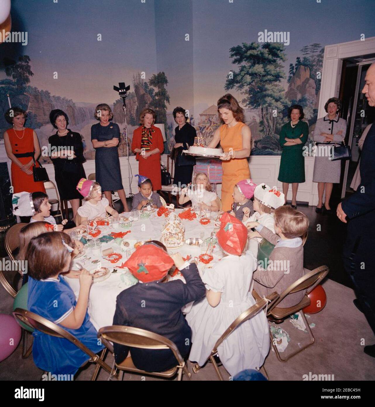 Festa di compleanno per Caroline Kennedy e John F. Kennedy, Jr. La First Lady Jacqueline Kennedy porta la torta Caroline Kennedyu0027s al tavolo durante una festa di compleanno congiunta per Caroline e John F. Kennedy, Jr. Avery Hatcher, figlio del Segretario della Stampa associato, Andrew T. Hatcher, siede a sinistra di Caroline; Maria Shriver (con retro alla telecamera) siede a sinistra in primo piano. Anche nella foto: Janet Auchincloss; maggiordomo della Casa Bianca, John W. Ficklin. Presidentu2019s Dining Room (Residence), Casa Bianca, Washington, D.C. Foto Stock