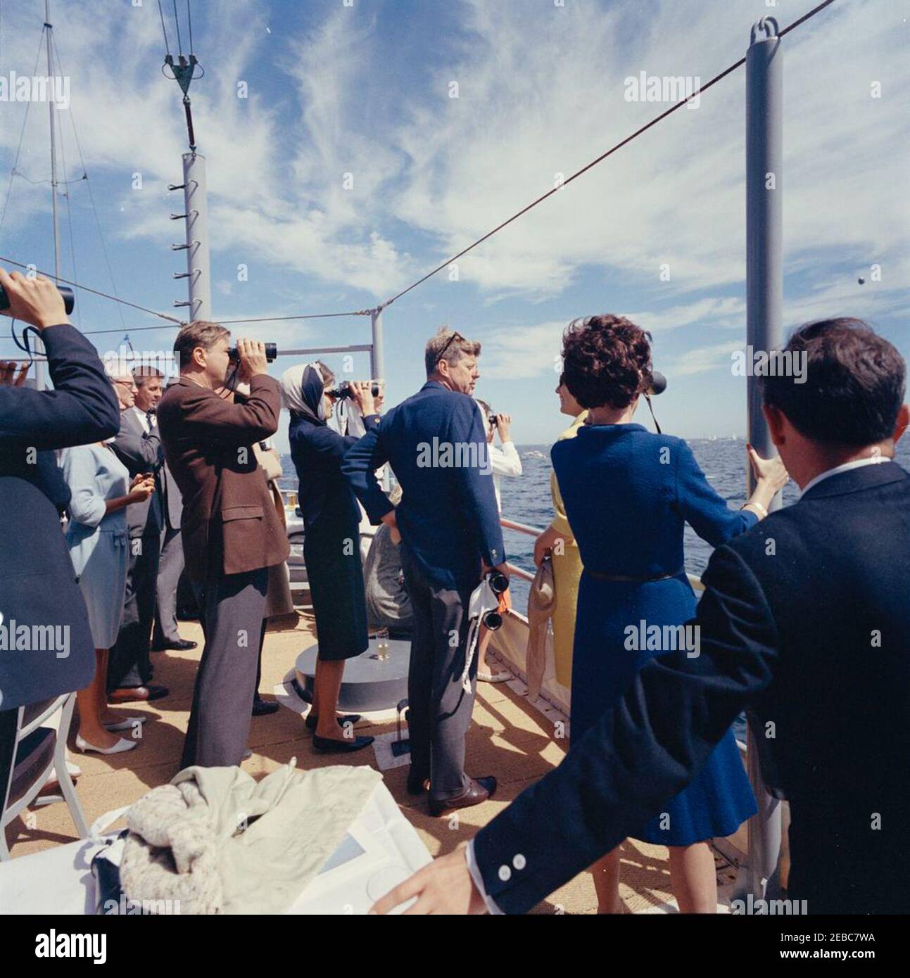 Il presidente Kennedy si accuda alla prima gara di Coppa Americau0027s. Il presidente John F. Kennedy e la First Lady Jacqueline Kennedy (entrambi al centro) guardano la prima gara della Americau0027s Cup 1962 a bordo della USS Joseph P. Kennedy, Jr. Anche nella foto: Anita Fay (moglie del Sottosegretario della Marina, Paul u0022Redu0022 Fay); il senatore John Sherman Cooper (Kentucky); Senatore Benjamin A. Smith II (Massachusetts); Franklin D. Roosevelt, Jr.; Barbara Mechem Smith; Janet Jennings Auchincloss. Newport, Rhode Island. Foto Stock