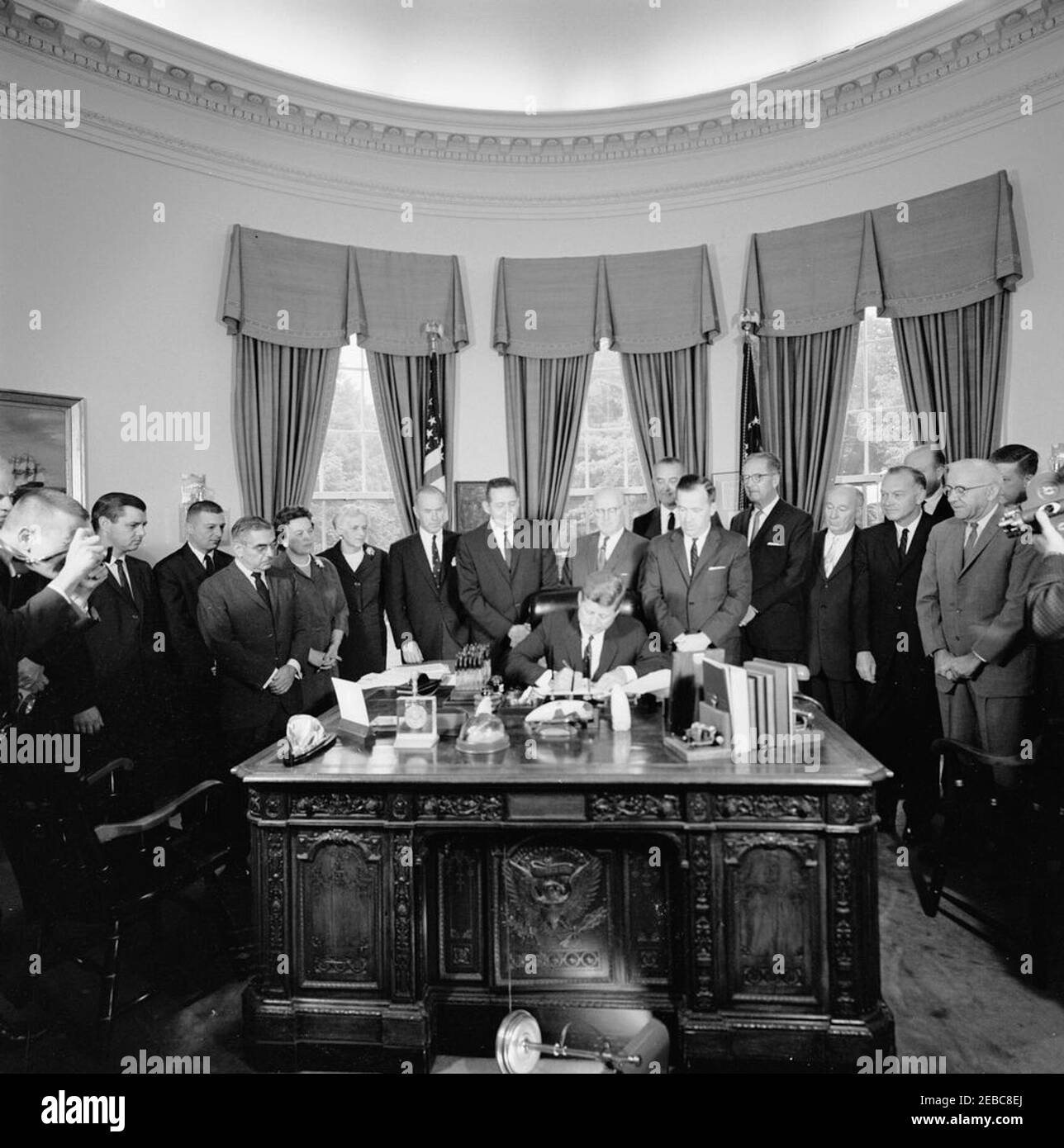 Firma della fattura - S.R. 11974 Legge pubblica 87-701, autorizzazione della Commissione dell'energia atomica (AEC) per 1963, 12:09PM. Il presidente John F. Kennedy (seduto alla scrivania) firma la legge di autorizzazione della Commissione per l'energia atomica (AEC) per il 1963. Guardando sopra (L-R): Fotografo di United Press International (UPI), James K. W. Atherton; due uomini non identificati; senatore John O. Pastore (Rhode Island); rappresentanti Catherine May, Julia Butler Hansen, e Jack Westland (tutti di Washington); rappresentante Craig Hoscher (California); presidente del Comitato congiunto per l'energia atomica, rappresentante Chet Holifield (California); Vic Foto Stock