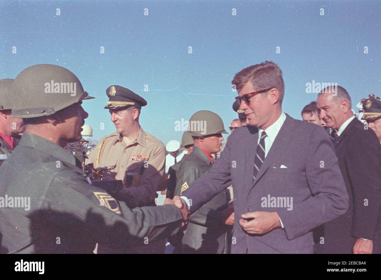 Viaggio negli Stati occidentali: White Sands Missile Range, New Mexico. Il presidente John F. Kennedy (indossando occhiali da sole) scuote le mani con il sergente Harman di prima classe D. Swits, III (a sinistra), che ha presentato al presidente Kennedy un modello in scala del missile sergente alla catena missilistica White Sands a White Sands, New Mexico; il presidente ha visitato White Sands per assistere a dimostrazioni missilistiche. Anche nella foto: Military Aide al presidente, General Chester V. Clifton (che detiene il modello missilistico sergente); Sergeant prima Classe Jimmie Grimes; Vice Presidente Lyndon B. Johnson. [Vedi anche MO 63.2019, u0022Modello di Serge Foto Stock