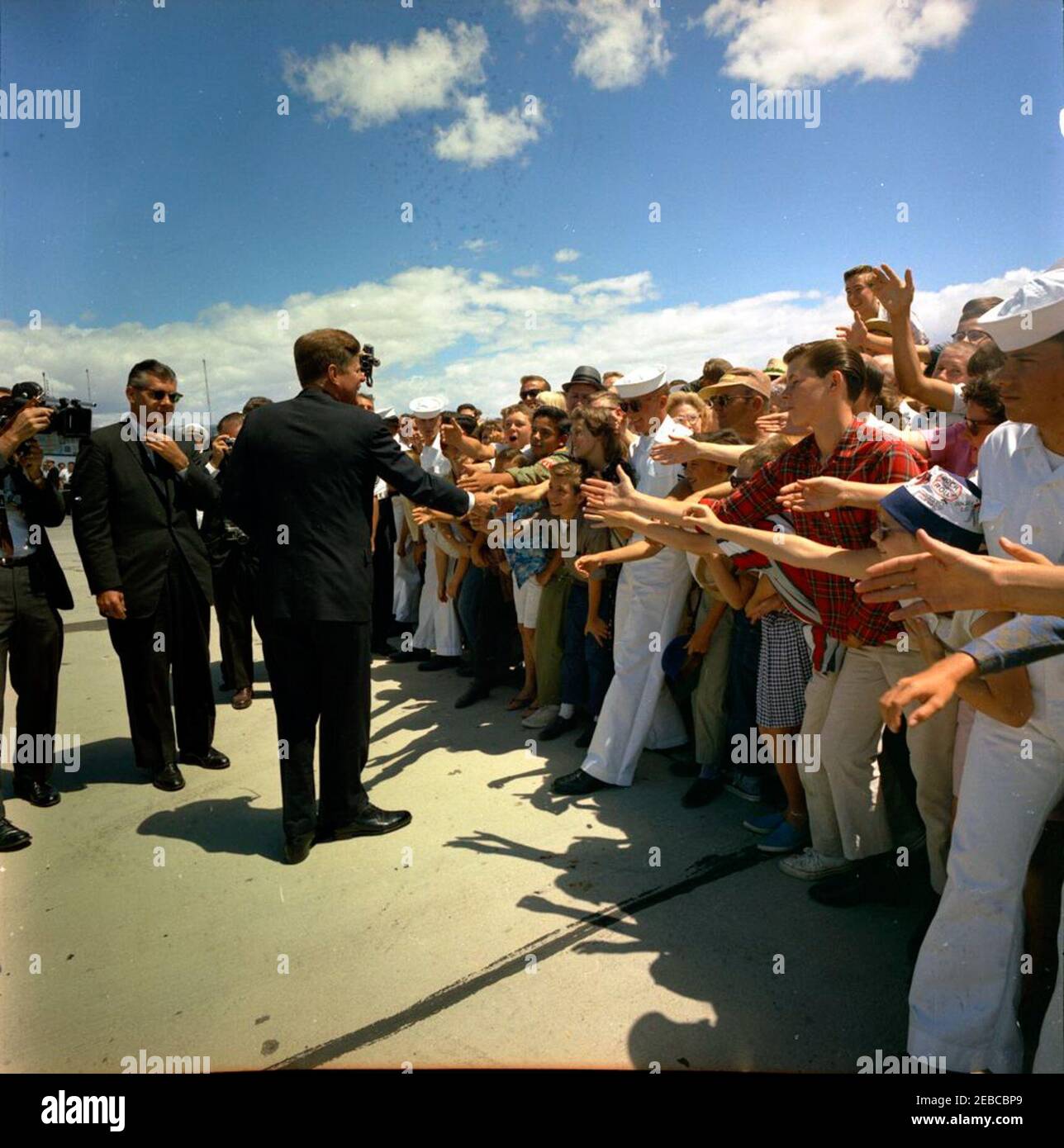 Viaggio negli stati occidentali: China Lake, California, (Naval Air Facility) NAF. Il presidente John F. Kennedy (a sinistra, con la mano estesa) saluta gli spettatori riuniti durante la sua visita alla base di prova navale dell'aeronautica (NAF) China Lakeu0027s (NOTS) nel lago cinese, California; l'agente di servizio segreto della Casa Bianca, Gerald A. u0022Jerryu0022 Behn, si trova sulla sinistra. Foto Stock