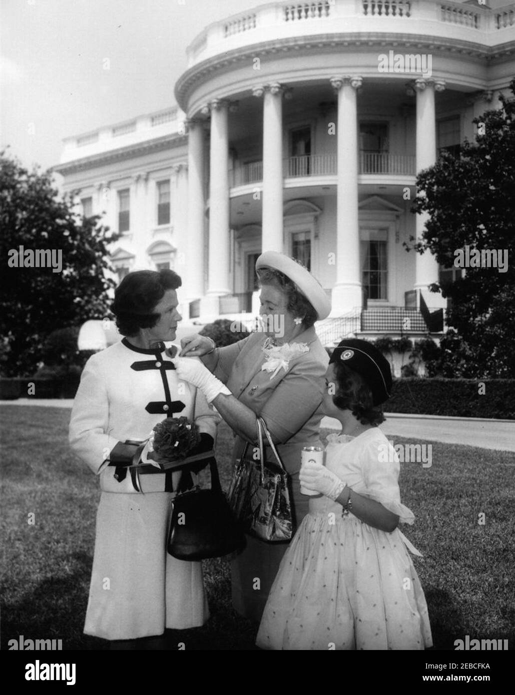 Margaret McNamara, moglie del Segretario della Difesa, presenta Shirley McKay con il presidente e la prima donazione Ladyu0027s alla Legion Auxiliaryu0027s 1962 Poppy Drive. Una donna non identificata infila un papavero sul lapello di Margaret Craig McNamara (moglie del Segretario della Difesa Robert McNamara) dopo una cerimonia di apertura della Legione americana Auxiliaryu2019s Poppy Drive 1962 a beneficio di veterani e orfani di guerra. A destra si trova Shirley McKay, di otto anni, di Broomall, Pennsylvania, un membro ausiliario junior. South Lawn, Casa Bianca, Washington, D.C. Foto Stock