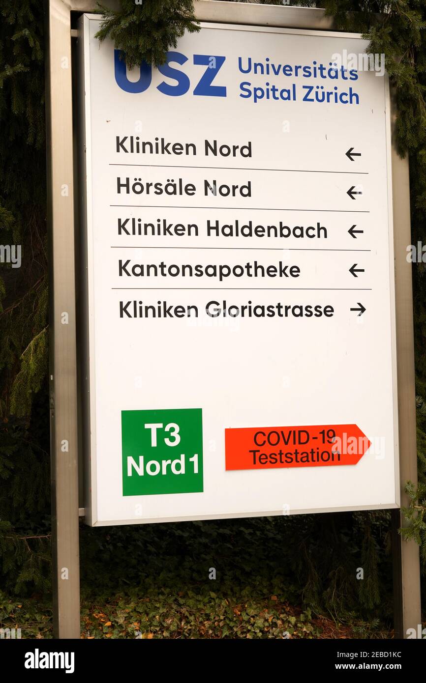 Segnaletica dell'Ospedale Universitario di Zurigo che mostra le indicazioni in tedesco e. un segno di direzione a forma di freccia arancione per il centro di test covid-19 o stazione di prova Foto Stock