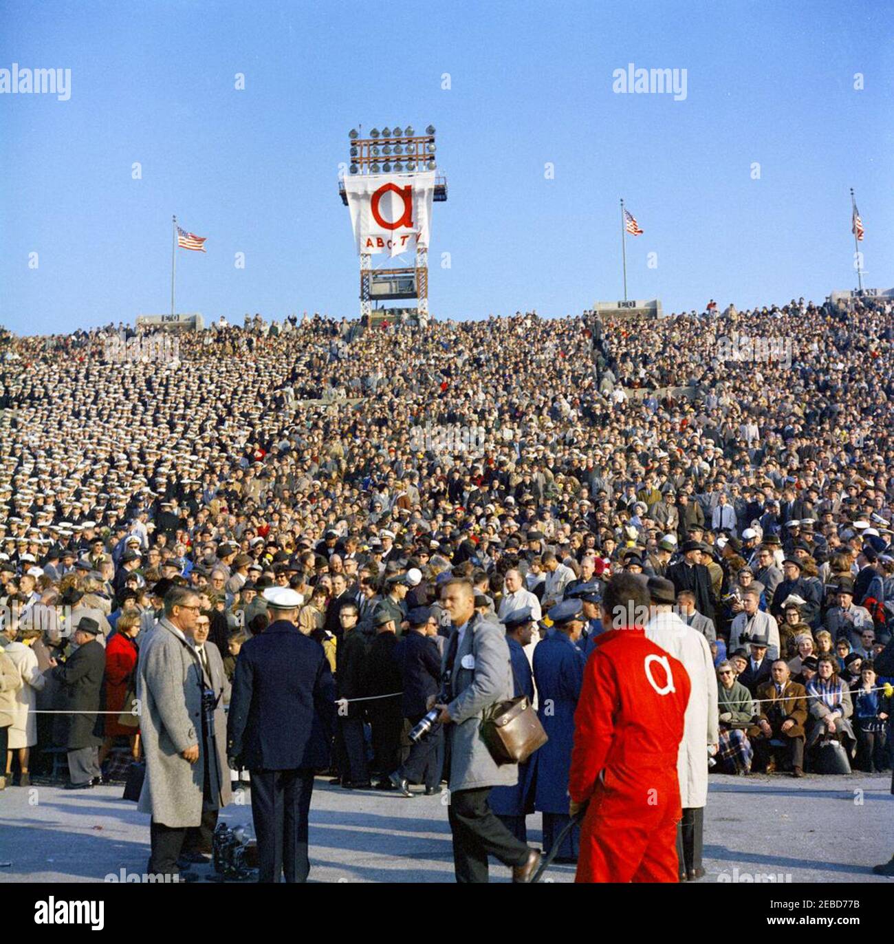 Army-Navy Football Game, Philadelphia, 13:30. Pubblico nel lato della Marina degli stand al gioco di Calcio Army-Navy (United States Military Academy Cadets contro United States Naval Academy Midshipmen), cui ha partecipato il presidente John F. Kennedy. Il fotografo di United Press International, James K. W. Atherton, si erge in primo piano (tenendo la fotocamera). Stadio municipale, Philadelphia, Pennsylvania. Foto Stock