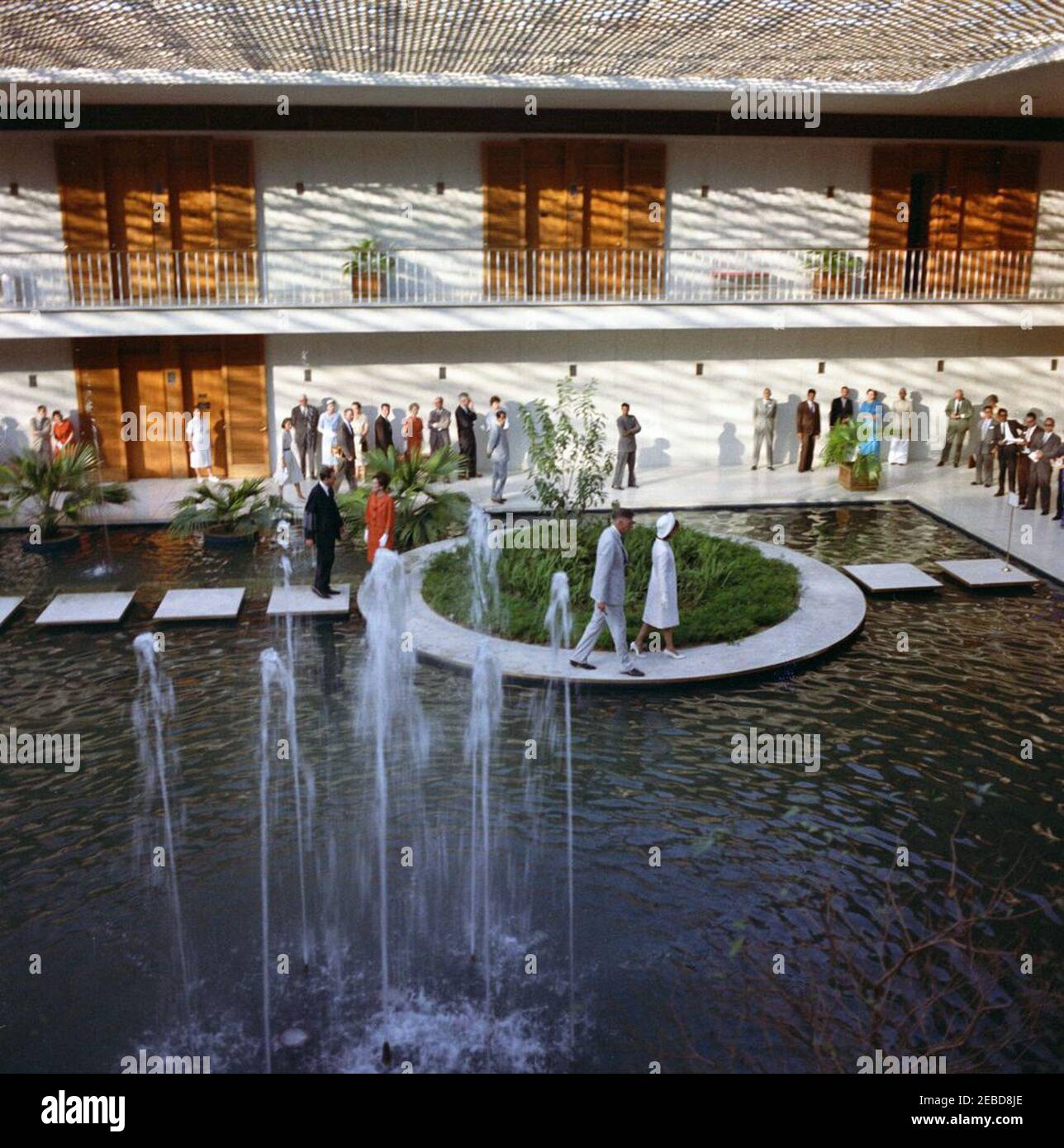Prima Lady Jacqueline Kennedyu2019s (JBK) viaggio in India e Pakistan: Nuova Delhi, Delhi, India, visita alla Chancery statunitense. First Lady Jacqueline Kennedy (centro a destra) cammina con l'Ambasciatore degli Stati Uniti in India John Kenneth Galbraith attraverso una piscina cortile presso la cancelleria dell'Ambasciata degli Stati Uniti a Nuova Delhi, India. La sorella della signora Kennedyu2019s, la principessa Lee Radziwill della Polonia, si trova a sinistra (indossando la tuta arancione). Foto Stock