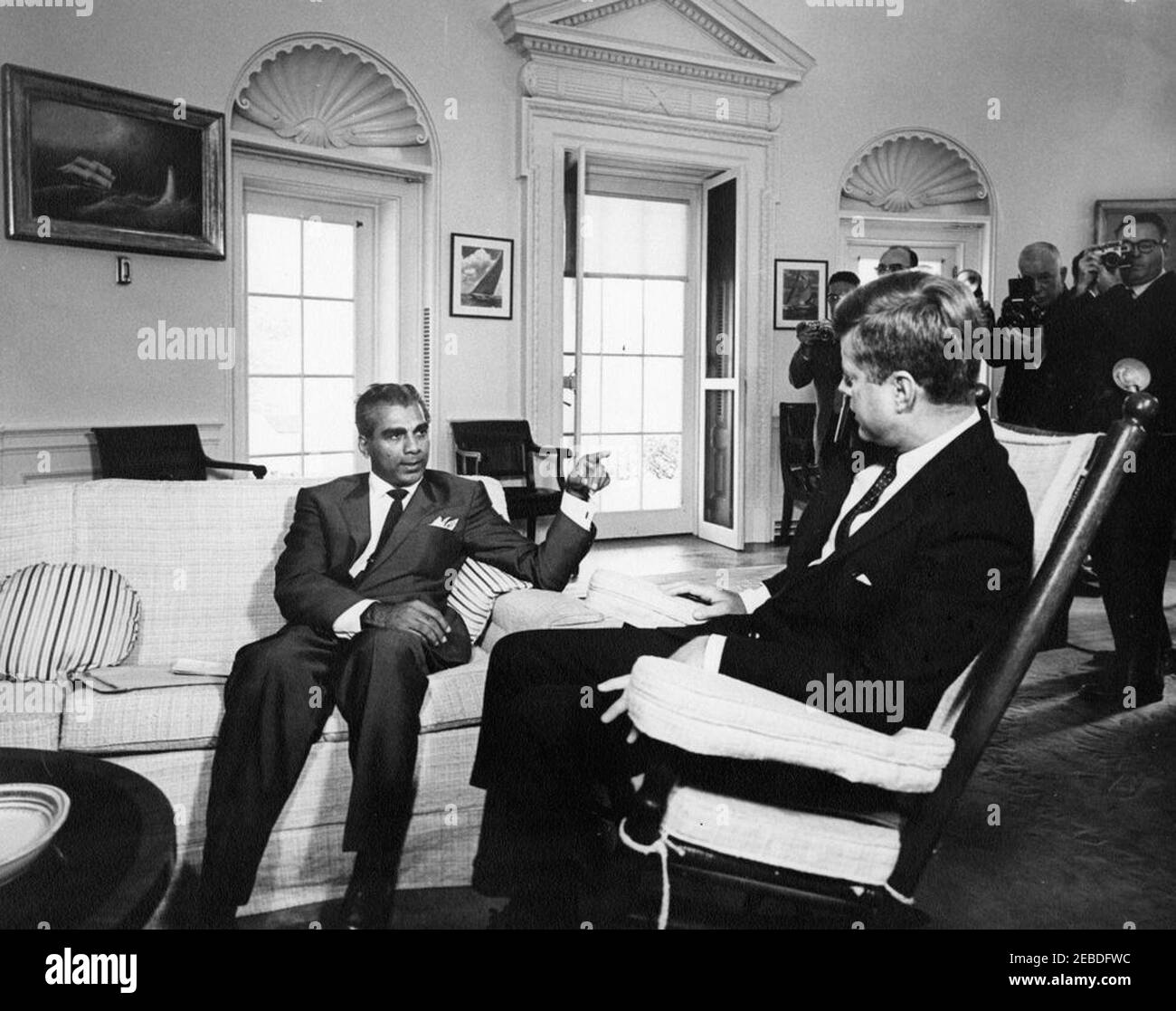 Incontro con Cheddi Jagan, Premier della Guiana Britannica, 00:11. Il presidente John F. Kennedy (in sedia a dondolo) incontra il dottor Cheddi Jagan, Premier della Guiana Britannica. I fotografi non identificati si levano in piedi sullo sfondo. Ufficio ovale, Casa Bianca, Washington, D.C. Foto Stock