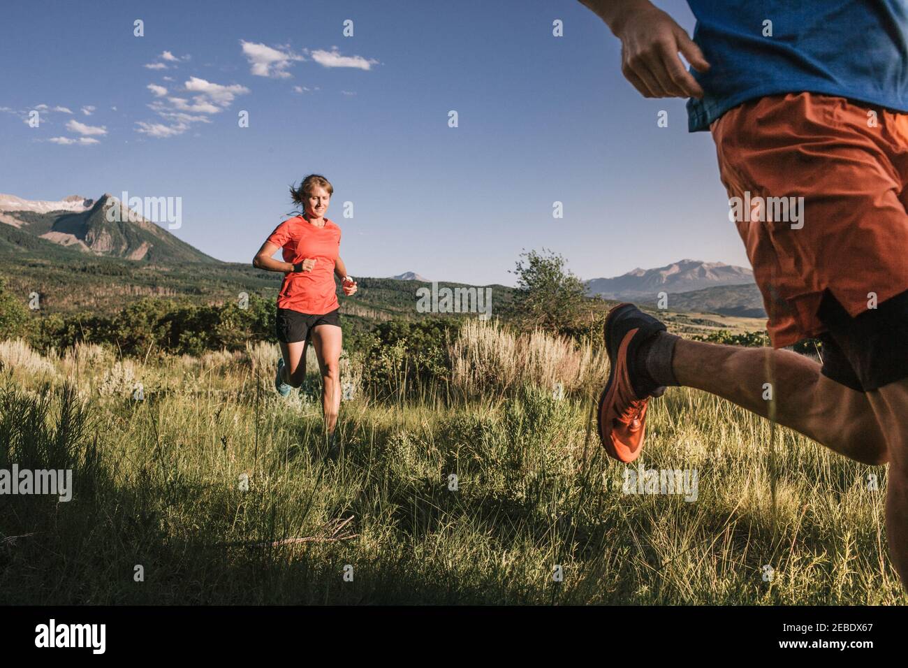 Due corridori di sentiero sprint attraverso l'erba alta campo con montagna visualizza Foto Stock