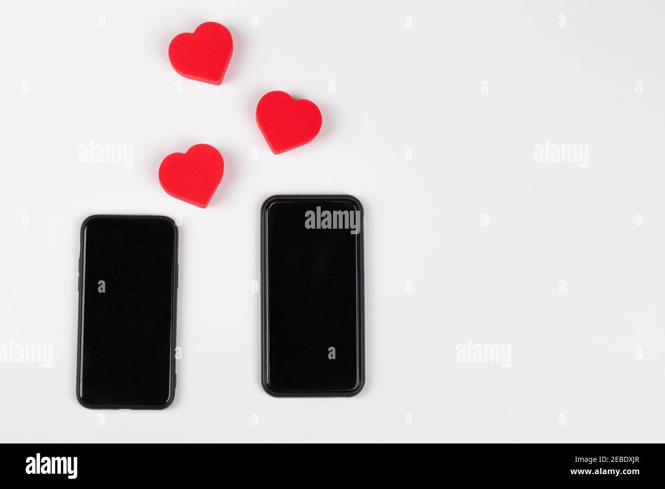Cuori rossi e due telefoni cellulari su sfondo bianco. Internet dating, copy space, concetto di giorno di San Valentino. Foto Stock