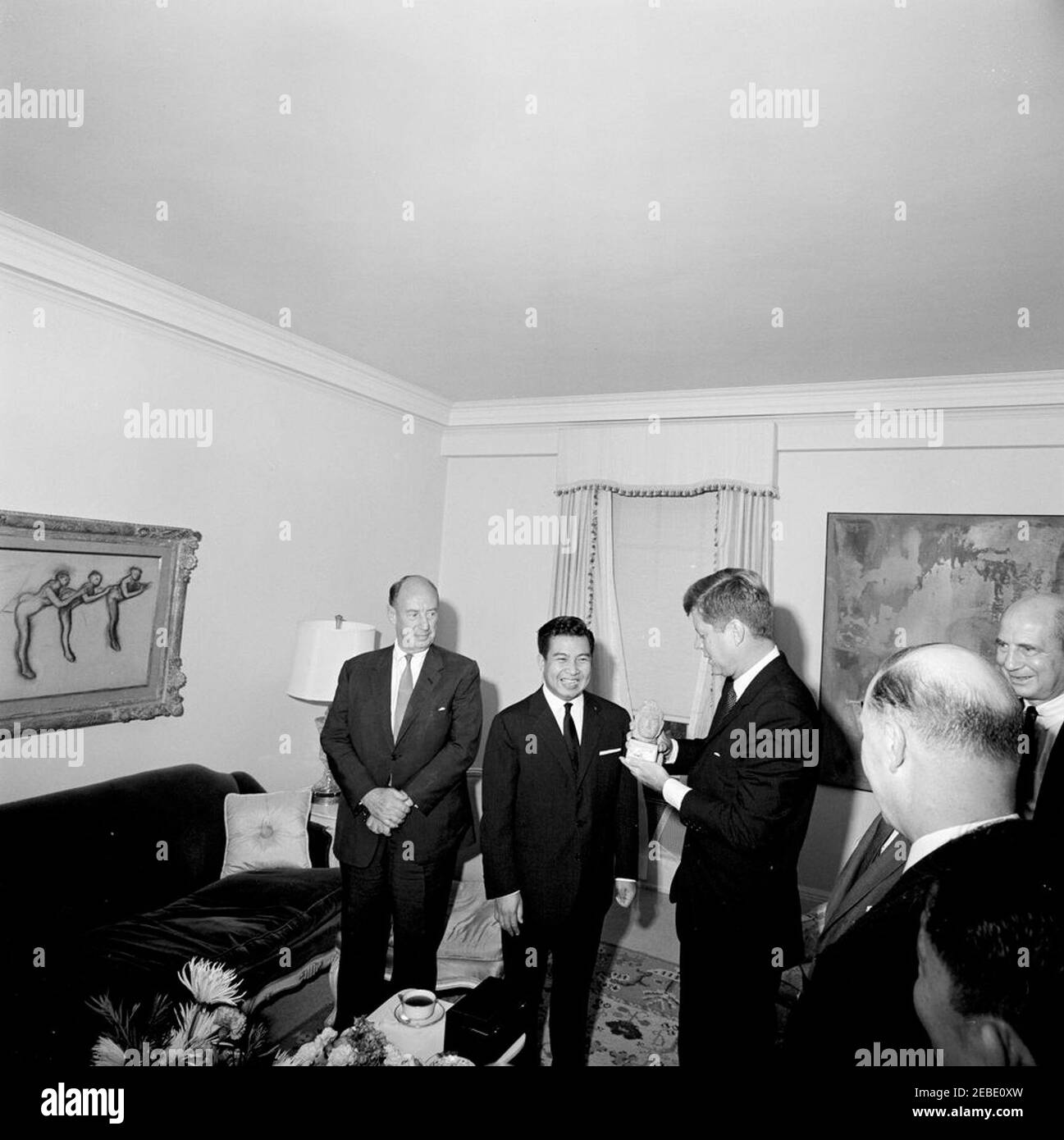 Viaggio a New York: Incontro con il Principe Norodom Sihanouk di Cambogia, alle 16:00. Il presidente John F. Kennedy detiene una piccola statua presentata dal principe Norodom Sihanouk della Cambogia nella Suite del Presidente 2019s al Carlyle Hotel, New York City, New York. (L-R) Ambasciatore degli Stati Uniti presso le Nazioni Unite Adlai Stevenson; Principe Sihanouk; Presidente Kennedy; John Steeves, Vice Segretario di Stato aggiunto per gli Affari dell'Estremo Oriente (di ritorno alla camera); Ambasciatore degli Stati Uniti in Cambogia William Trimble. Ambasciatore della Cambogia Nong Kinny (parzialmente fuori quadro) è in basso a destra. Foto Stock