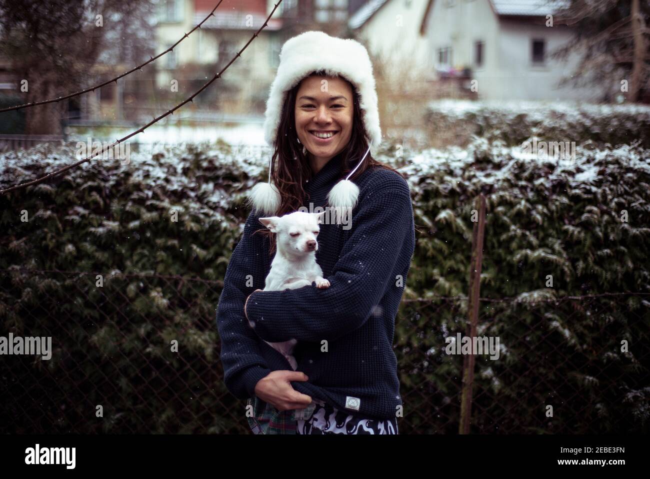 Donna asiatica sorride a macchina fotografica bianco morbido cappello e. cane bianco Foto Stock