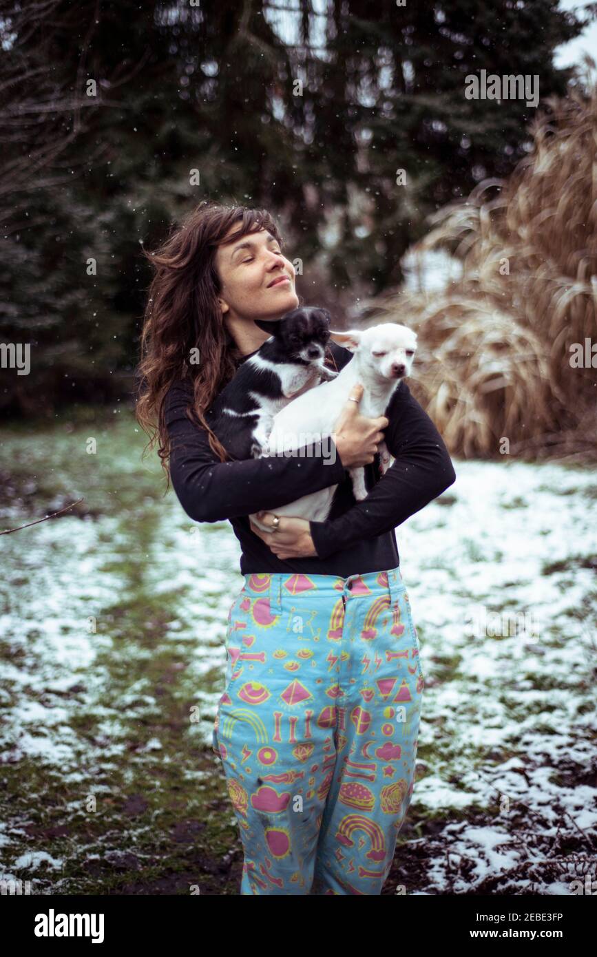 donna felice attraverso testa indietro nella neve che tiene due piccoli cani in cortile Foto Stock
