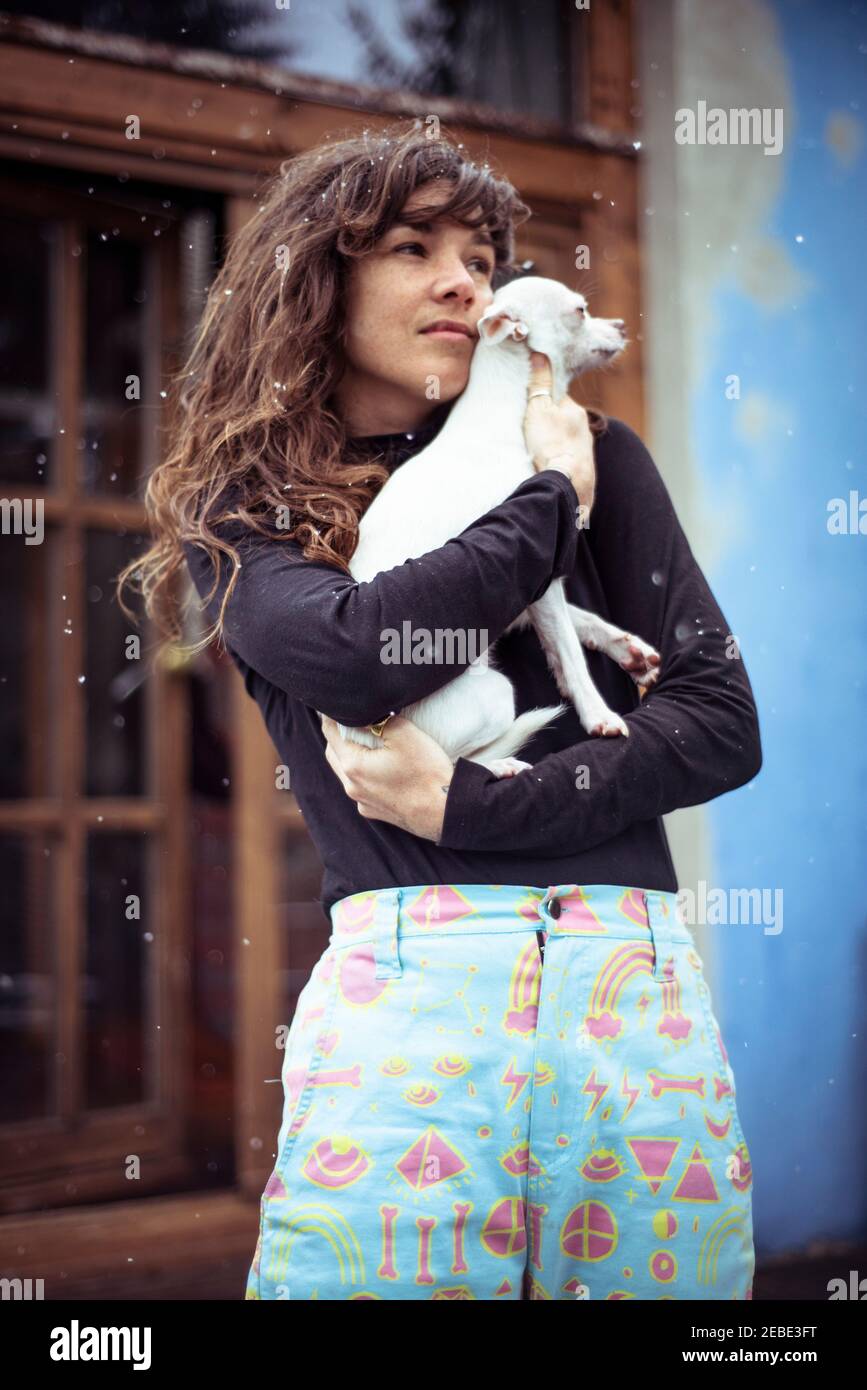 Donna con neve nei capelli tiene il piccolo cane bianco a. tieniti caldo all'aperto Foto Stock