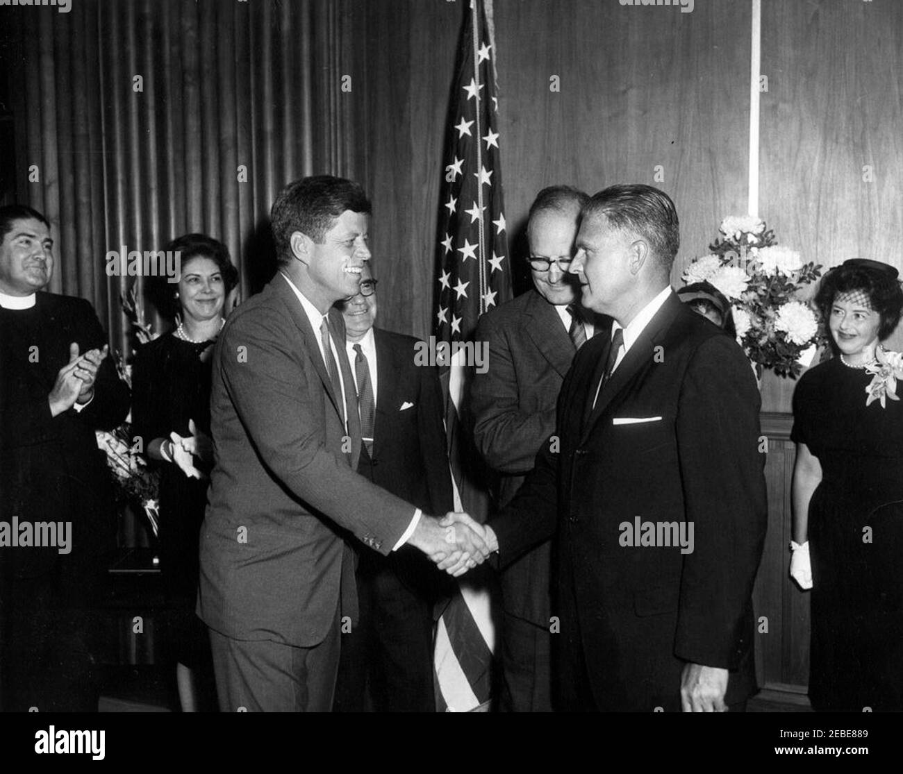 Cerimonia di giuramento, James J. Rowley, Direttore del Servizio Segreto, 10:37. Il presidente John F. Kennedy stringe le mani con il nuovo direttore del servizio segreto James J. Rowley alla cerimonia di giuramento del direttore Rawelyu2019 presso il Dipartimento del Tesoro di Washington, D.C. (L-R) il direttore Raweleyu2019, il fratello Francis P. Rowley; la sorella Marge Rowley Borise del direttore Raweleyu2019; il presidente John F. Kennedy; l'impiegato non identificato (parzialmente nascosto); Segretario del Tesoro C. Douglas Dillon; Direttore Rowley; Direttore Roweyu2019s moglie Mabel Rita Cluen Rowley. Foto Stock
