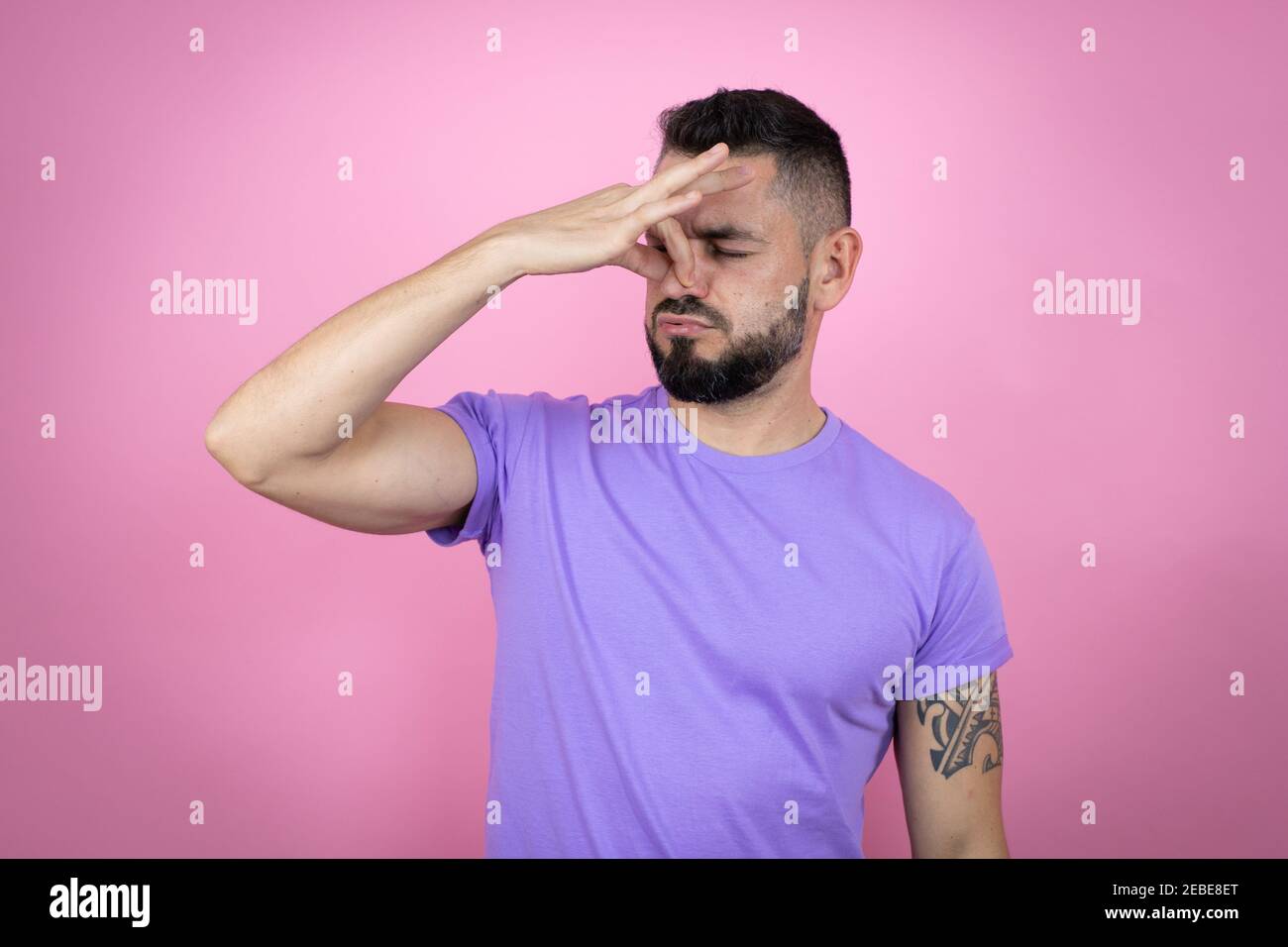 Giovane bell'uomo che indossa una t-shirt casual su sfondo rosa odore qualcosa di stinoso e disgustoso, odore intollerabile, trattenendo il respiro con le dita Foto Stock