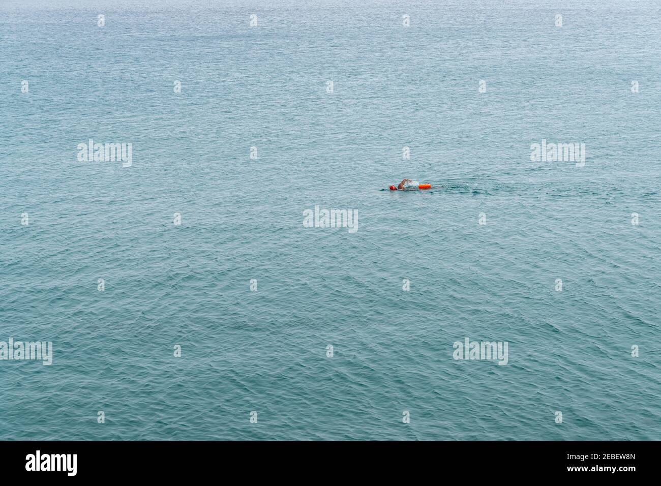 Nuotatore a lunga distanza con cappuccio arancione e borsa a secco in acqua oceano aperta senza fine Foto Stock