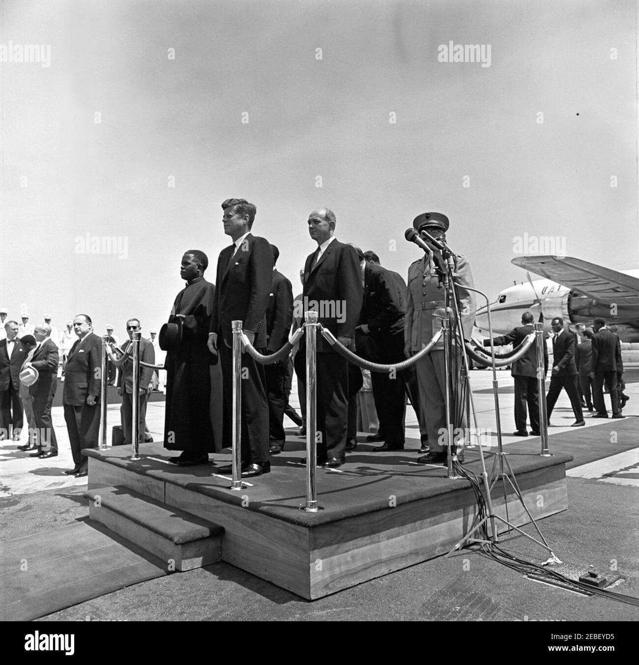 Cerimonia di arrivo per Fulbert Youlou, Presidente della Repubblica del Congo (Brazzaville), ore 12. Cerimonia di arrivo per il Presidente della Repubblica del Congo (Brazzaville) Fulbert Youlou. Sulla piattaforma (L-R): Presidente Youlou, Presidente John F. Kennedy, Ambasciatore della Repubblica del Congo (Brazzaville) Emmanuel Damongo Dadet, Segretario di Stato Dean Rusk, Capo del Dipartimento di Stato del protocollo Angier Biddle Duke, e Comandante del corpo Marino degli Stati Uniti David M. Shoup (dietro i microfoni). Nella foto sono inclusi anche Assian, che si trova a sinistra della piattaforma Foto Stock