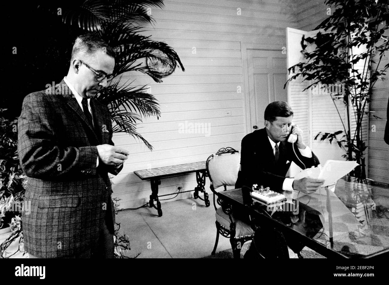 Cerimonia di apertura della fiera di Seattle Worldu0027s da Palm Beach. Il presidente John F. Kennedy rilascia le sue osservazioni per telefono prima di premere un tasto del telegrafo d'oro (sul tavolo del patio) per aprire la fiera di Seattle Worldu0027s del 1962 (conosciuta anche come esposizione del secolo 21) via segnale satellitare dalla residenza di C. Michael Paul a Palm Beach, Florida. Robert Bright, della American Telephone and Telegraph Company (ATu0026T), si trova a sinistra. Foto Stock