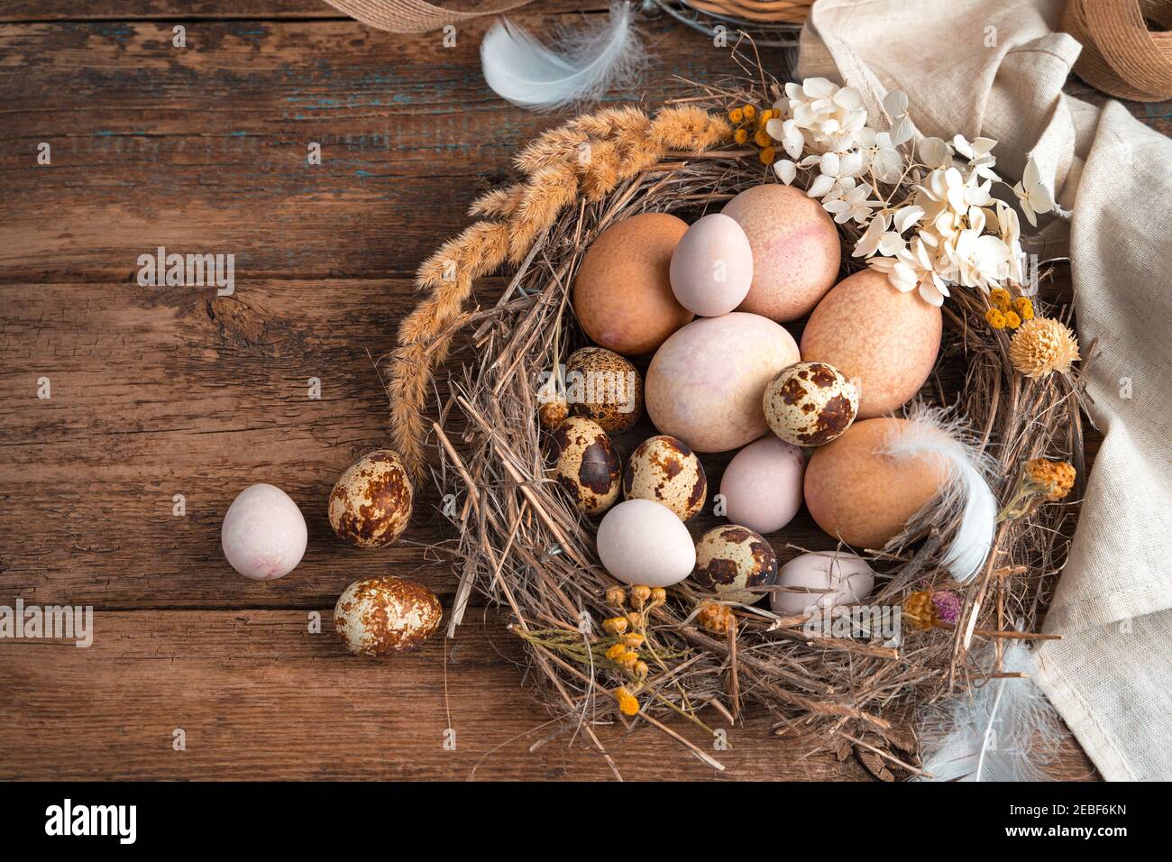 Pasqua vintage sfondo. Le uova di quaglia e le uova di pollo giacciono in un nido di vimini, decorato con fiori e piume. Foto Stock