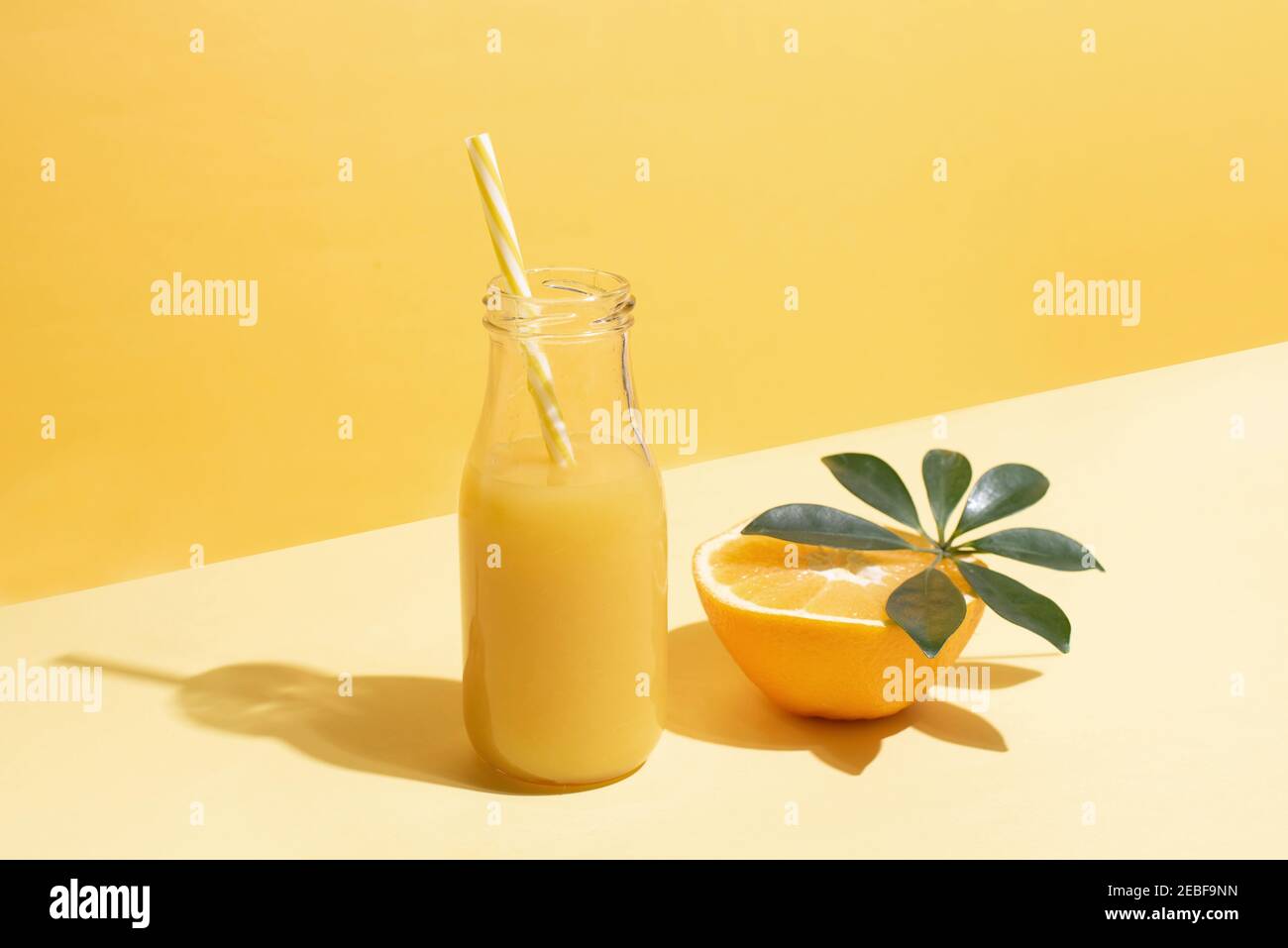 Una bottiglia con succo d'arancia e mezzo d'arancia e una cannuccia su sfondo giallo ai raggi del sole, isometrica, primo piano. Concetto estivo. Foto Stock