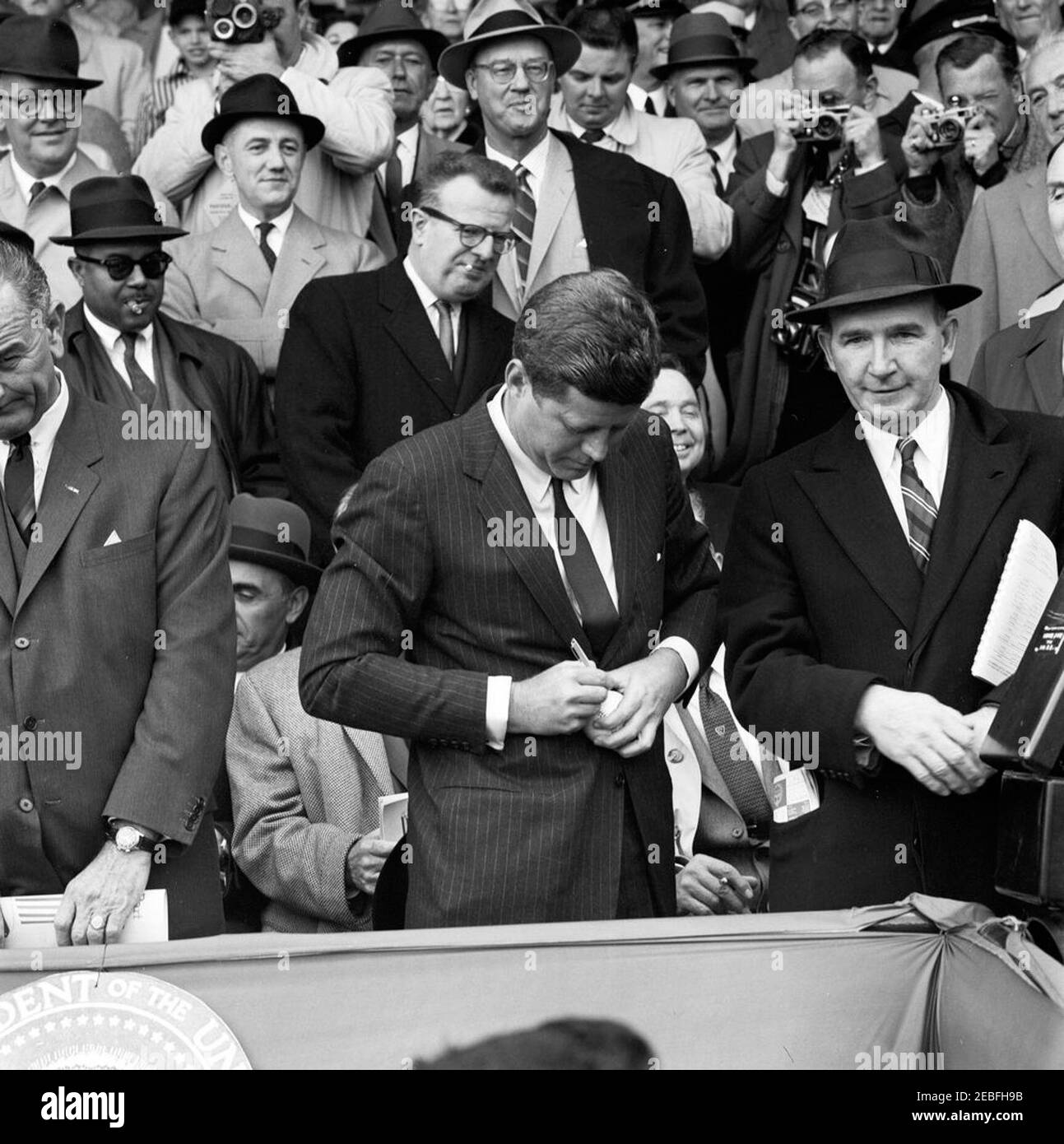 Giorno di apertura della stagione di baseball 1961, 13:10. Il presidente John F. Kennedy firma un baseball alla partita di apertura della stagione di baseball 1961 al Griffith Stadium di Washington, D.C. il pubblico comprende il vicepresidente Lyndon B. Johnson; il segretario alla stampa associato Andrew Hatcher; l'assistente speciale al presidente Lawrence u0022Larryu0022 Ou0027Brien; il rappresentante Carl Albert dell'Oklahoma; Assistente speciale al Presidente Dave Powers. Foto Stock