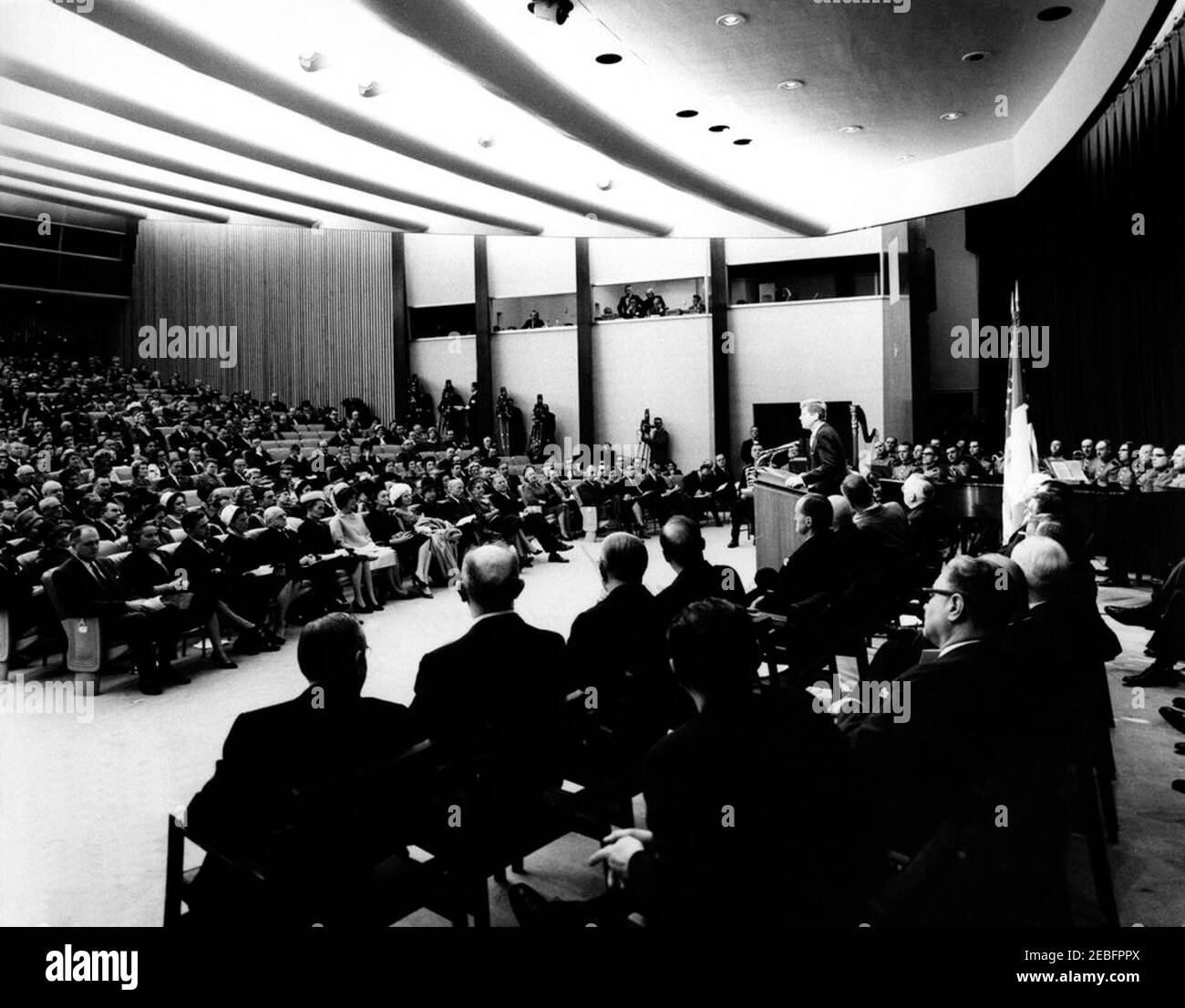 Cerimonia di celebrazione dell'unità d'Italia, 10:31. Cerimonia di celebrazione dell'unità d'Italia. Ampio scatto dell'auditorium, dal lato del palco; il presidente John F. Kennedy parla dal leggio; i partecipanti ascoltano mentre siediti nel pubblico e nella tribuna della parla2019; First Lady Jacqueline Kennedy, in prima fila di spettatori; I membri della United States Marine Band si trovano all'estremità destra del palco. Auditorium del Dipartimento di Stato, Washington, D.C. Foto Stock