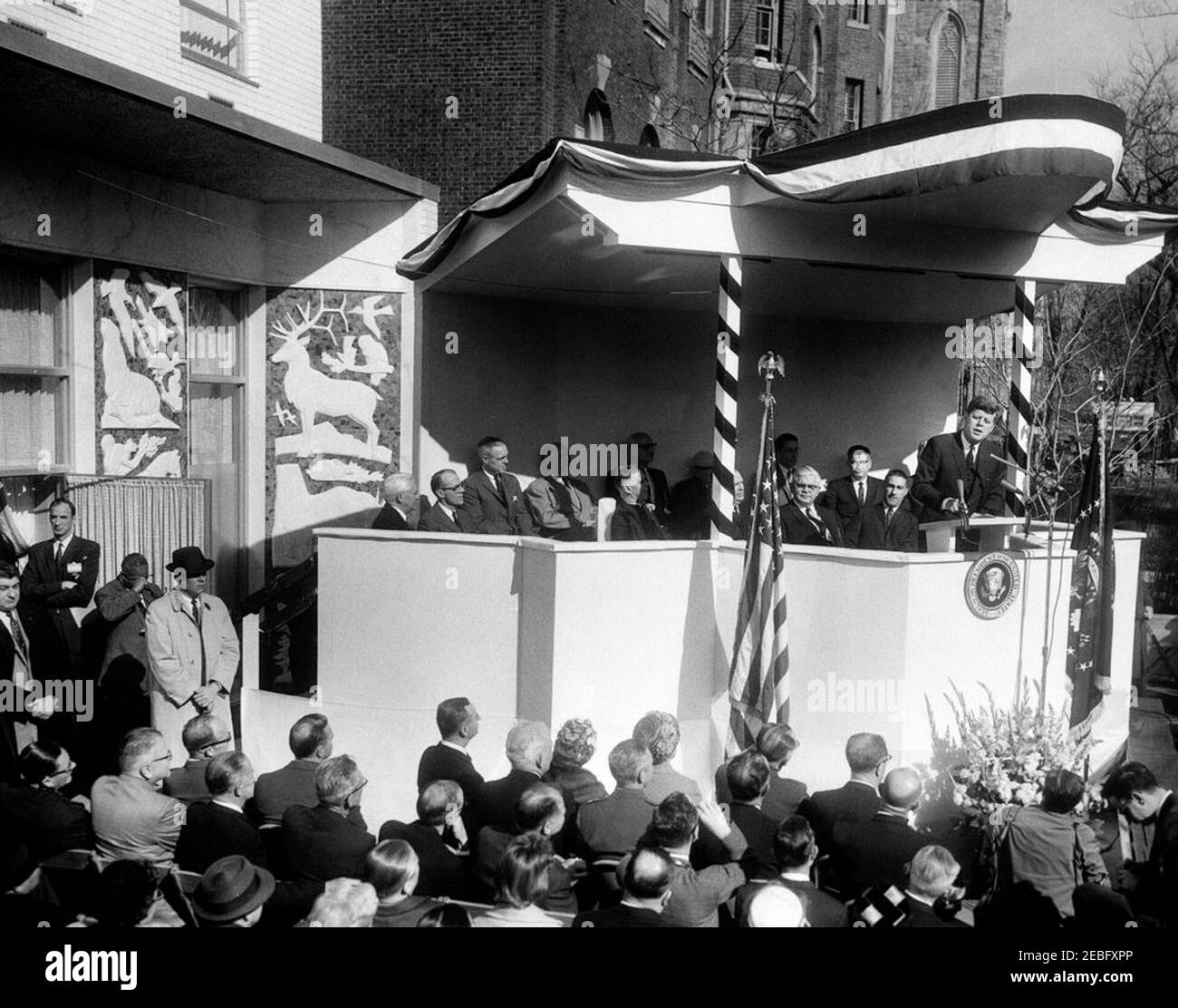 Cerimonia di dedica, National Wildlife Federation (NWF) Building a Washington, D.C., 9:30. Il presidente John F. Kennedy parla ad una cerimonia di dedicazione per il National Wildlife Federation Building. Anche nella foto: Segretario dell'interno Stewart Udall (a sinistra del presidente); Direttore della National Wildlife Federation (NWF) e Maestro delle cerimonie, giudice Lewis D. McGregor (seduto a destra della bandiera americana); Presidente della National Wildlife Federation, Claude B. Kelley (seduto tra il fascio sul lato sinistro e la bandiera americana); il reverendo Frederick Brown Harris (seduto in prima fila del relatore Foto Stock