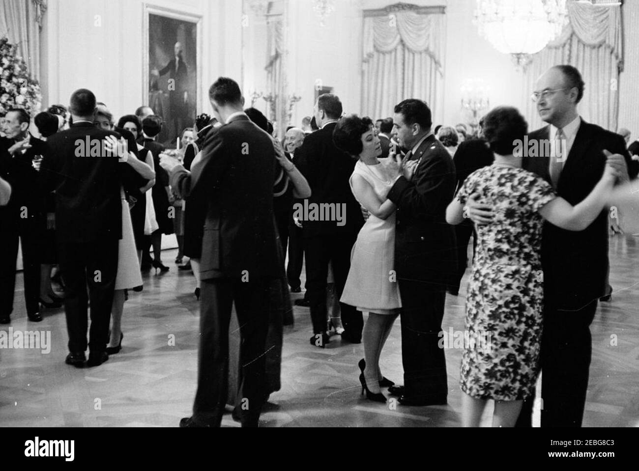 Accoglienza diplomatica alle 18:00. Gli ospiti ballano presso un ricevimento diplomatico presso la Casa Bianca. Il Segretario dell'interno, Stewart Udall (di ritorno alla macchina fotografica), balla con sua moglie, Erma Lee Udall, all'estrema sinistra; Air Force Aide al presidente, Brigadier General Godfrey T. McHugh, danza con una donna non identificata al centro destra; Ambasciatore dell'Unione Sovietica (URSS), Anatoloy Fedorovich Dobrynin, danza con sua moglie, Irina Nikolaevna, all'estrema destra. Tutti gli altri non sono identificati. Camera Est, Casa Bianca, Washington, D.C. Foto Stock