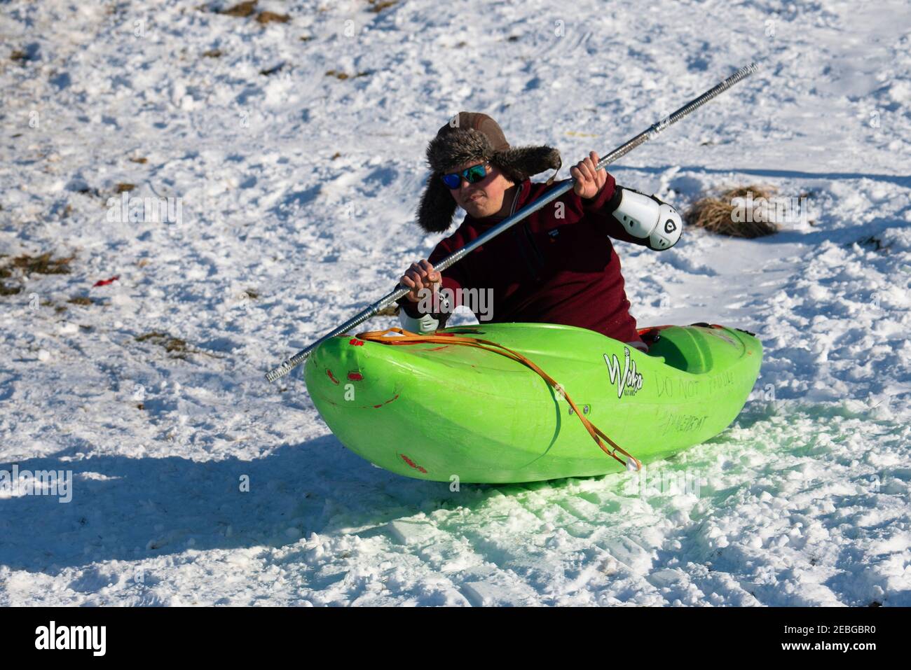 L'uomo in kayak scivola lungo la collina innevata di Holyrood Park, Edimburgo, Scozia, Regno Unito Foto Stock