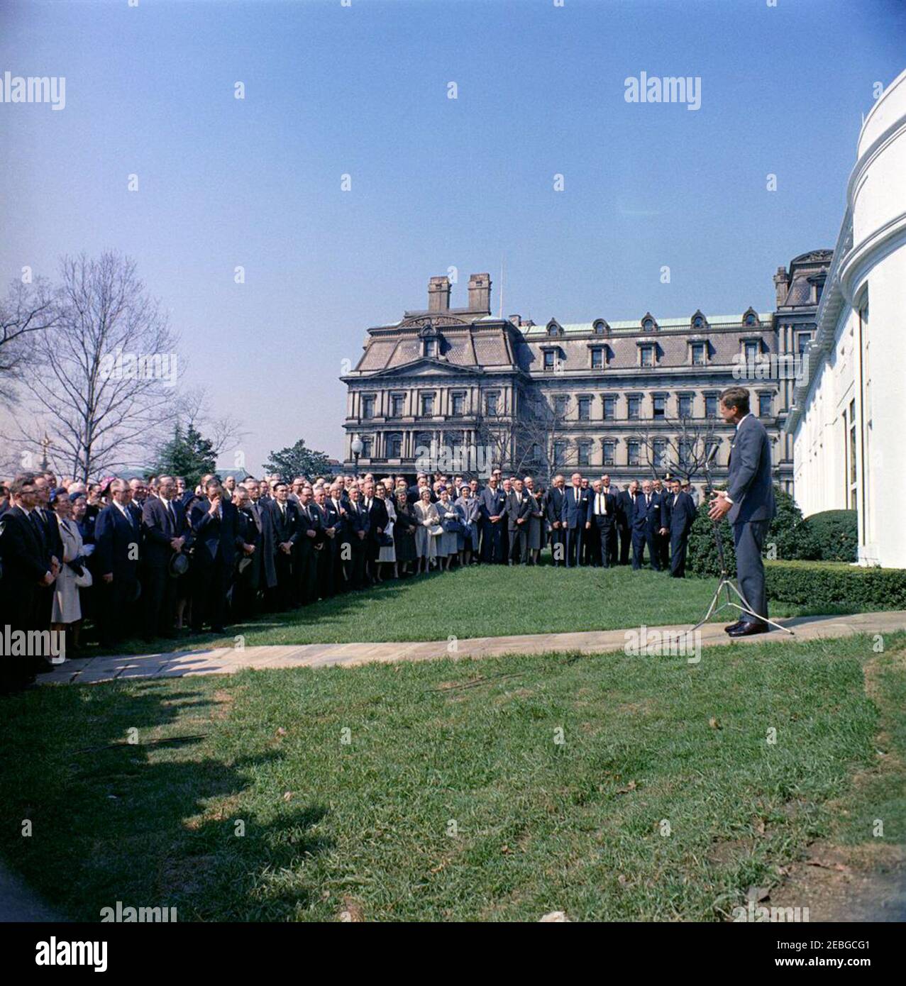 Incontro con i membri della stabilizzazione agricola u0026 Comitati di conservazione, 9:45. Il presidente John F. Kennedy (destra) si rivolge ai membri dei comitati di stabilizzazione e conservazione agricola (ASC) sul prato dell'ala ovest della Casa Bianca, Washington, D.C. l'edificio dell'ufficio esecutivo è visibile sullo sfondo. Foto Stock