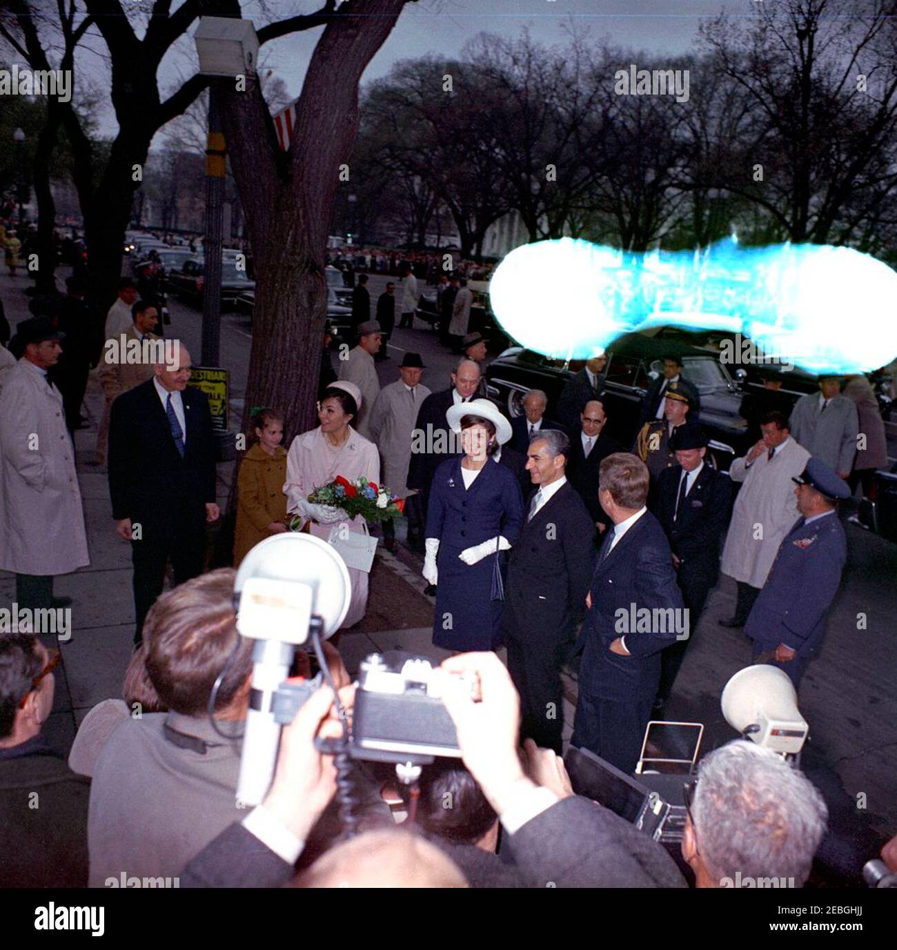 Cerimonia di arrivo per lo Scià dell'Iran, Mohammad Reza Shah Pahlavi, 12:00. Il presidente John F. Kennedy (a destra, di fronte) e la First Lady Jacqueline Kennedy (al centro, con cappello bianco) stanno con Mohammad Reza Pahlavi, lo Shahanshah dell'Iran (a sinistra del presidente Kennedy), E sua moglie, l'imperatrice Farah Pahlavi (che tiene bouquet di fiori), sul marciapiede fuori Blair House, Washington, D.C. Vice Capo del protocollo William J. Tonesk si trova a sinistra dell'imperatrice; Assistente Segretario della stampa, Jay W. Gildner cammina dietro il vice Tonesk. Quelli che stanno dietro i capi di stato includono (L-R): Segreto Foto Stock