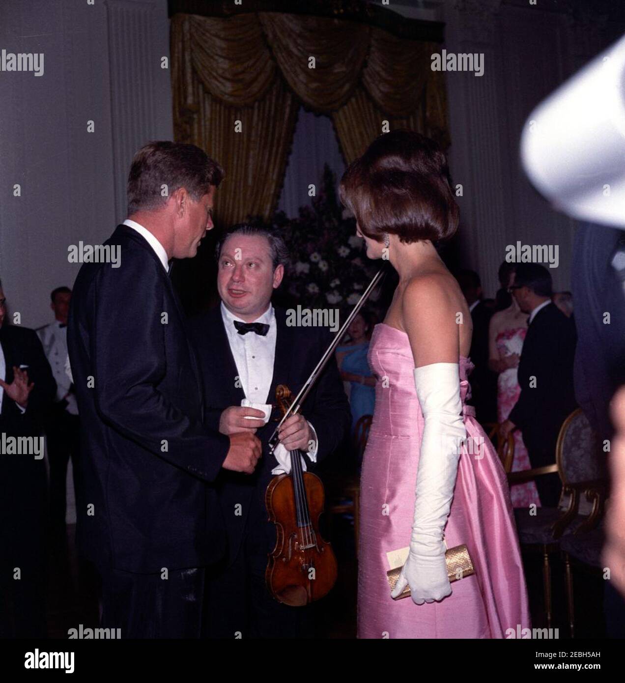 Cena in onore di Andru00e9 Malraux, Ministro degli Affari culturali della Francia, alle 20:00. Il presidente John F. Kennedy e la prima signora Jacqueline Kennedy visitano il violinista Isaac Stern, dopo la sua esibizione in una cena in onore del ministro francese per gli affari culturali, Andru00e9 Malraux. Anche nella foto (sullo sfondo): Helen Olson Wirth (moglie del Direttore del Servizio del Parco Nazionale (NPS), Conrad L. Wirth); corrispondente della Casa Bianca per il Columbia Broadcasting System (CBS), George Herman, e sua moglie, Patricia Herman. Camera Est, Casa Bianca, Washington, D.C. Foto Stock