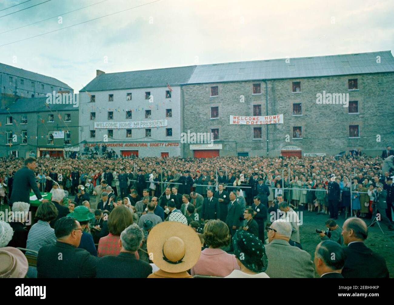 Viaggio in Europa: Irlanda, New Ross. Il presidente John F. Kennedy (a sinistra, al leggio) ha un discorso prima che la folla si riunì a New Ross Quay a New Ross, nella contea di Wexford, Irlanda, il porto da cui il suo bisnonno, Patrick Kennedy, emigrò negli Stati Uniti. Giornalisti e fotografi osservano dal basso la piattaforma speakersu0027; anche nella foto (seduta sulla piattaforma speakersu0027): Vice Presidente del New Ross Urban District Council, Gerald Donovan; la sorella del Presidente Kennedyu0027s, Jean Kennedy Smith; la cognata del Presidente 0027s, la Principessa Lee Radziwill di Polonia; Presidente o Foto Stock