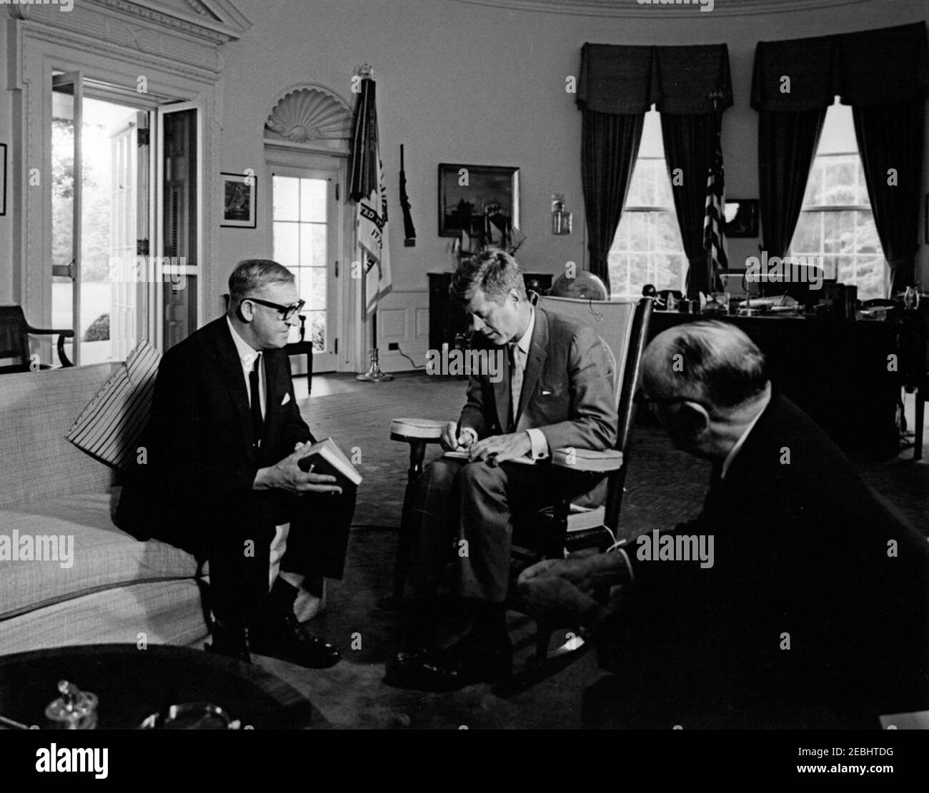 Incontro con Arthur A. Calwell, leader del Partito laburista d'Australia, ORE 12:05. Il presidente John F. Kennedy (in sedia a dondolo, scrivendo in un libro) incontra il leader del Partito laburista australiano Arthur A. Calwell (a sinistra, tenendo una penna e un libro); l'ambasciatore d'Australia, Sir Howard Beale (di nuovo alla macchina fotografica), siede a destra. Ufficio ovale, Casa Bianca, Washington, D.C. Foto Stock