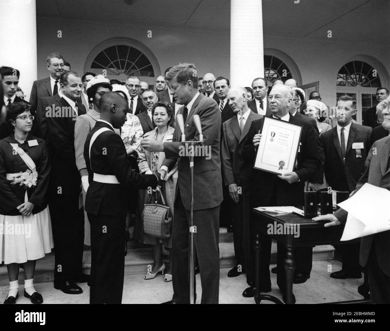 Presentazione dell'American Automobile Association (AAA) LifesSaving Awards nel Rose Garden, 9:50. Il presidente John F. Kennedy stringe le mani con Wayne Brown (di New York, New York) presentandolo con l'American Automobile Association (AAA) Lifesaving Award; quattro altri membri dell'Organisationu2019s School Safety Patrol hanno ricevuto anche il premio. Le foto includono: Premiati, John Puhak (di Hazelton, Pennsylvania) e Patricia Miller (di Hereford, Pennsylvania); il senatore George A. Smathers (Florida); il rappresentante George M. Rhodes (Pennsylvania); il senatore John O. Pastore Foto Stock