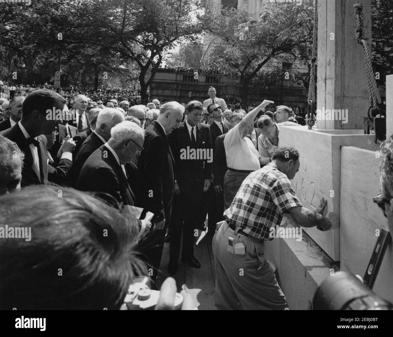 Cerimonia di posa Cornerstone, edificio degli uffici della Casa di Rayburn, 10:28. Il presidente John F. Kennedy osserva l'abbassamento di un blocco di marmo durante la cerimonia di posa della pietra angolare per l'edificio degli uffici della Rayburn House, dedicato al defunto Presidente della Camera dei rappresentanti, Sam Rayburn. Tra gli altri che stanno cercando: Rappresentante Roland V. Libonati (Illinois); architetto del Campidoglio, J. George Stewart; Presidente della Camera e Presidente della Commissione per la costruzione dell'Ufficio della Camera, John W. McCormack (Massachusetts); Rappresentante Samuel S. Stratton (New York); Rappresentante Charles MCC. Mathias, J. Foto Stock