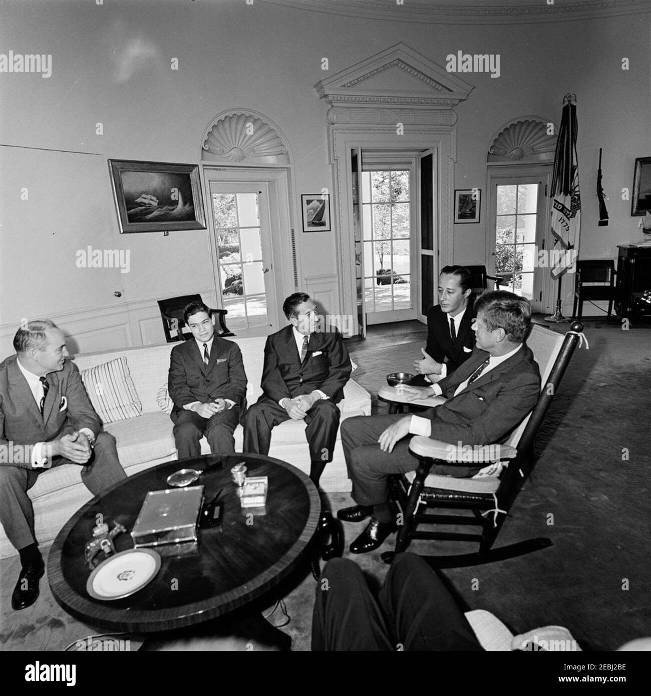 Incontro con Miguel Aleman, ex presidente del Messico, ore 10. Il presidente John F. Kennedy (in sedia a dondolo) incontra l'ex presidente del Messico, Miguel Alemu00e1n. Da sinistra a destra: Due non identificati; Alemu00e1n; interprete del Dipartimento di Stato, Donald Barnes; presidente Kennedy. Ufficio ovale, Casa Bianca, Washington, D.C. Foto Stock