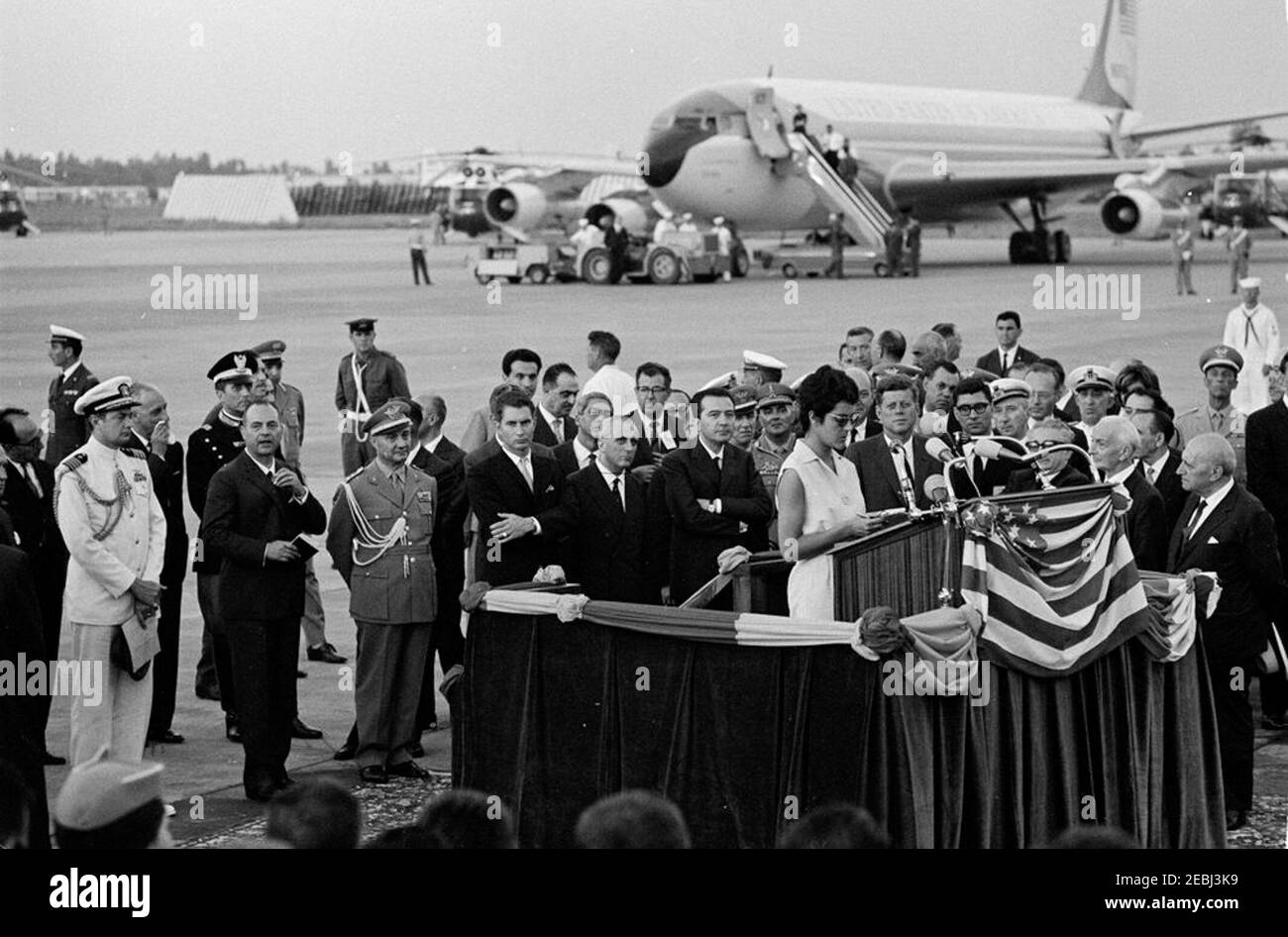 Viaggio in Europa: Italia, Napoli: Partenza del presidente Kennedyu2019, 18:30. Il presidente John F. Kennedy osserva come una donna non identificata si trova presso un leggio all'aeroporto di Capodichino a Napoli, Italia; il presidente Kennedy ha espresso osservazioni all'aeroporto prima di partire per gli Stati Uniti. Sempre nella foto: Presidente d'Italia, Antonio segni; primo Ministro d'Italia, Giovanni Leone; Aide Navale al Presidente Kennedy, Capitano Tazewell T. Shepard; Capo dello Stato di Difesa, Generale Aldo Rossi; Capo di protocollo italiano, Angelo Corrias; Ambasciatore d'Italia negli Stati Uniti, Sergio Fenoaltea; U. Foto Stock