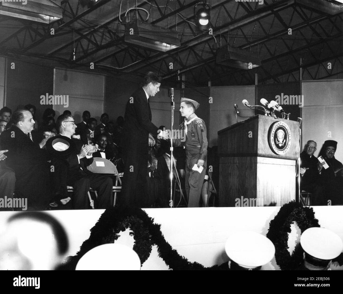 Cerimonia di illuminazione, albero di Natale nazionale all'Ellipse, 17:15. Il presidente John F. Kennedy scuote le mani con un Boy Scout da Wheaton, Maryland, all'illuminazione dell'albero di Natale Nazionale durante il Natale della capitale Nazionale Pageant of Peace all'Ellipse, il parco Presidentu2019s, Washington, D.C. seduto a sinistra del leggio, in prima fila (L-R): Ambasciatore del Nicaragua e Decano del corpo Diplomatico, Dr. Guillermo Sevilla-Sacasa; Sottosegretario agli interni, James K. Carr. I membri del coro del Tuskegee Institute, tra cui il direttore Relford Patterson, siedono sullo sfondo. Foto Stock