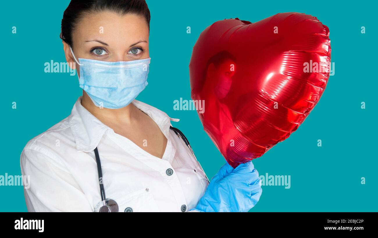 Una dottoressa con una maschera medica tiene un palloncino cuore rosso.  Concetto di cardiologia Foto stock - Alamy