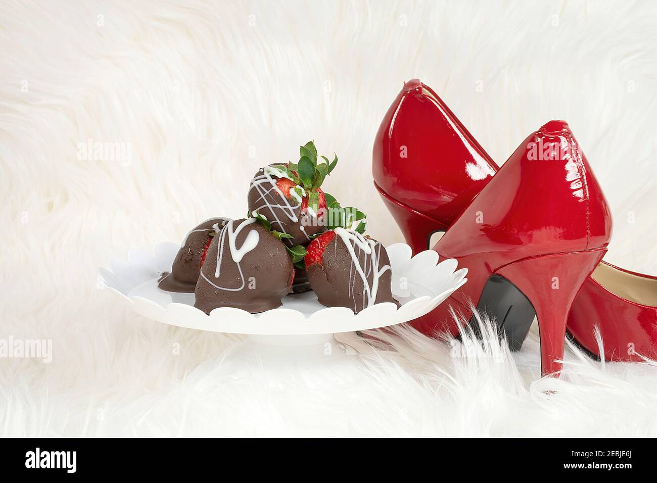 fragole ricoperte di cioccolato su piatto a piedistallo su pelliccia bianca con pompe rosse Foto Stock