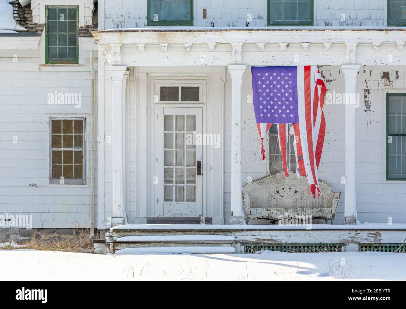 Bandiera americana infranto appesa verticalmente sul portico anteriore di una vecchia casa Foto Stock