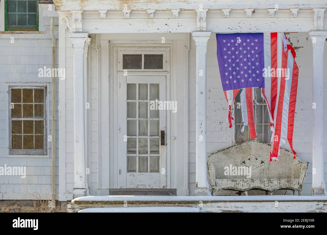 Bandiera americana infranto appesa verticalmente sul portico anteriore di una vecchia casa Foto Stock