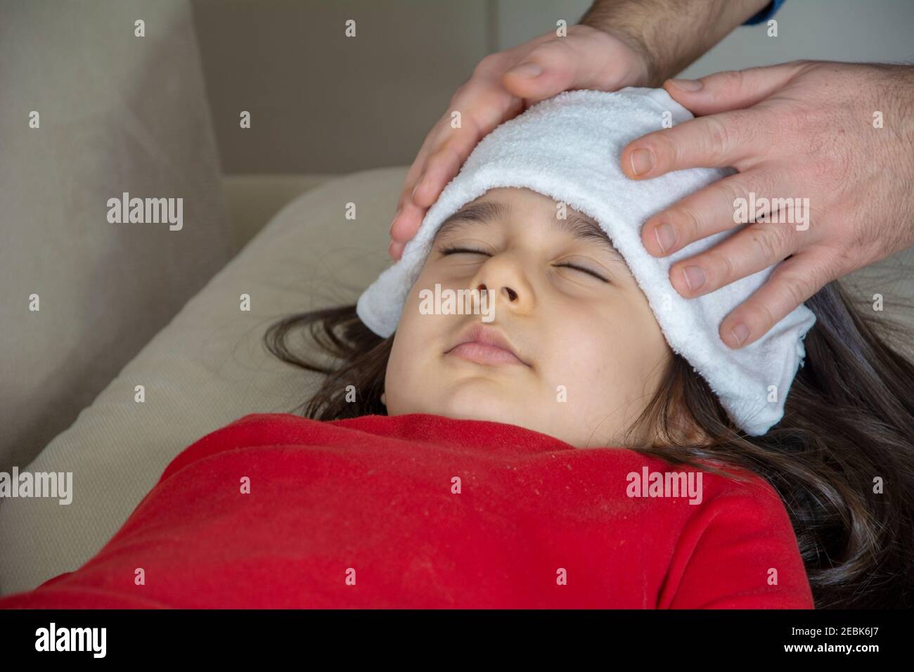 La mano di un uomo copre un panno umido sulla testa della ragazza che è malata in primo piano Foto Stock